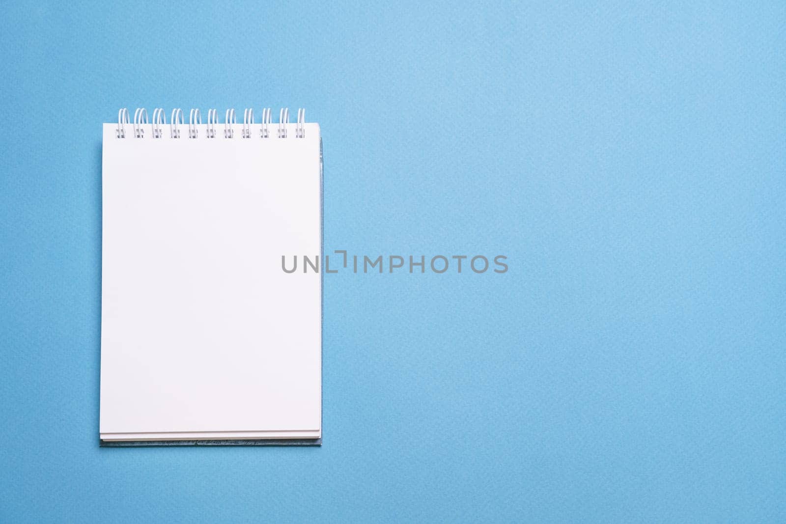 School notebook on blue background, spiral notepad on table, education by EkaterinaPereslavtseva