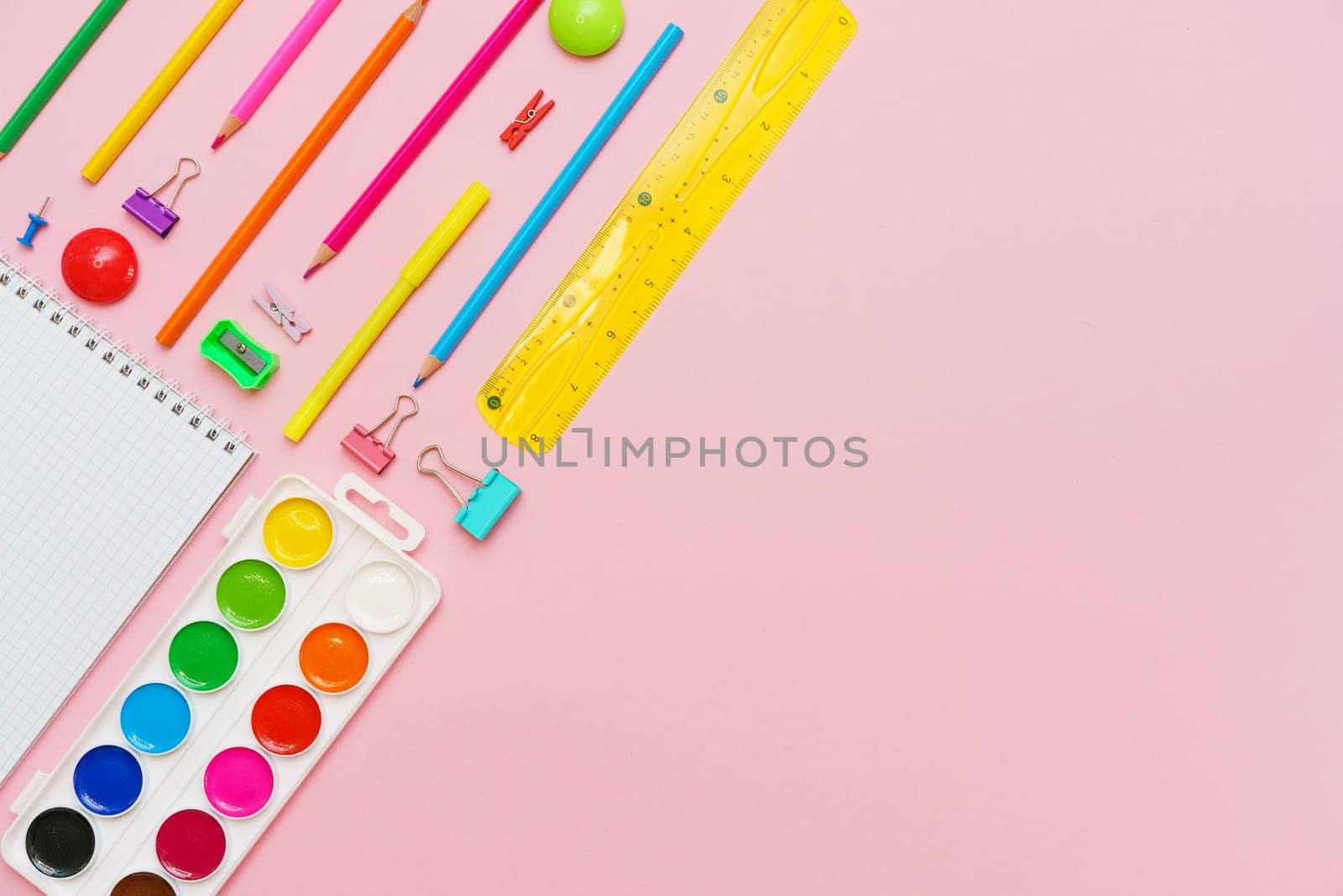 White notepad on spring and stationery school supplies on a pink background, heaps of colored pencils, paper clips, multi-colored objects for work and creativity, back to school