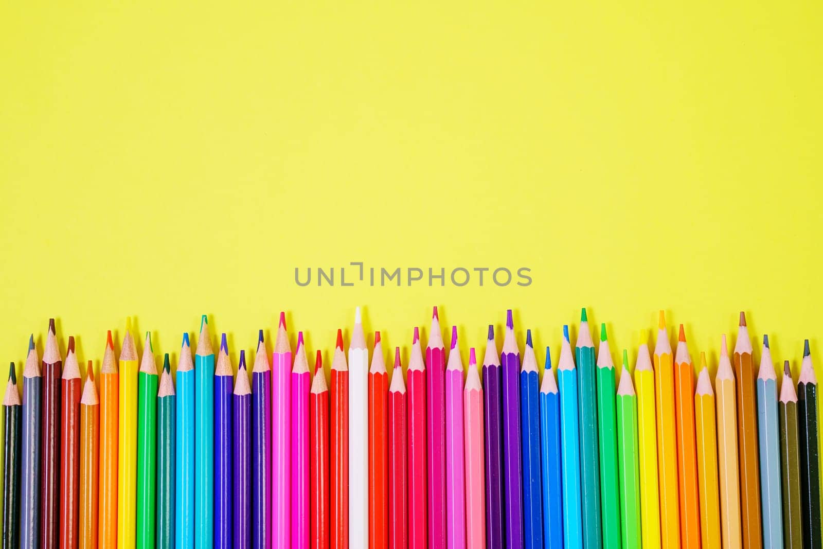 Assortment of colored pencils in various iridescent colors on a yellow background