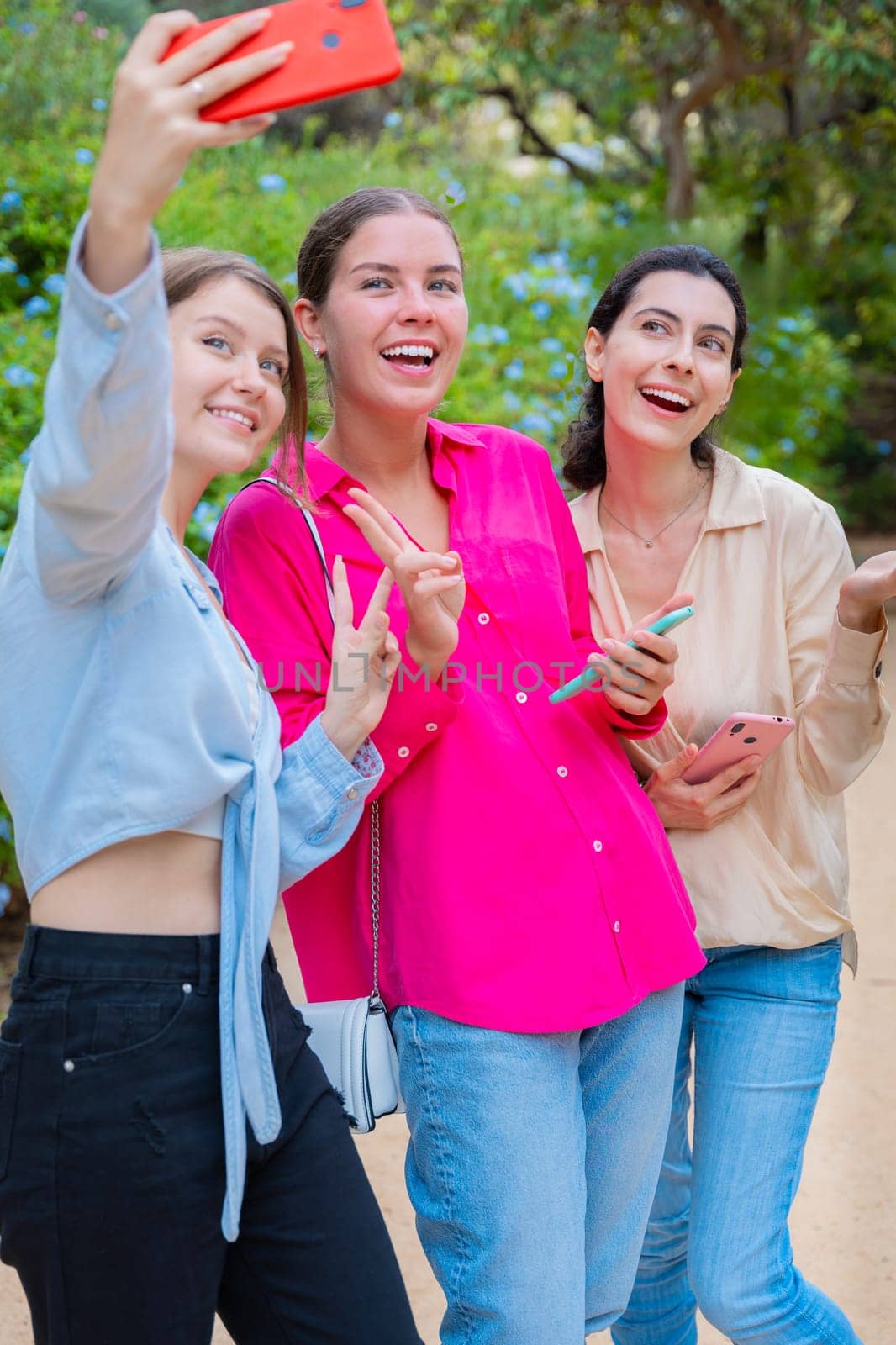 Three smiling women posing for a selfie in a lush green park. They embrace each other, expressing happiness and friendship. The vibrant colors and natural background create a joyful atmosphere.