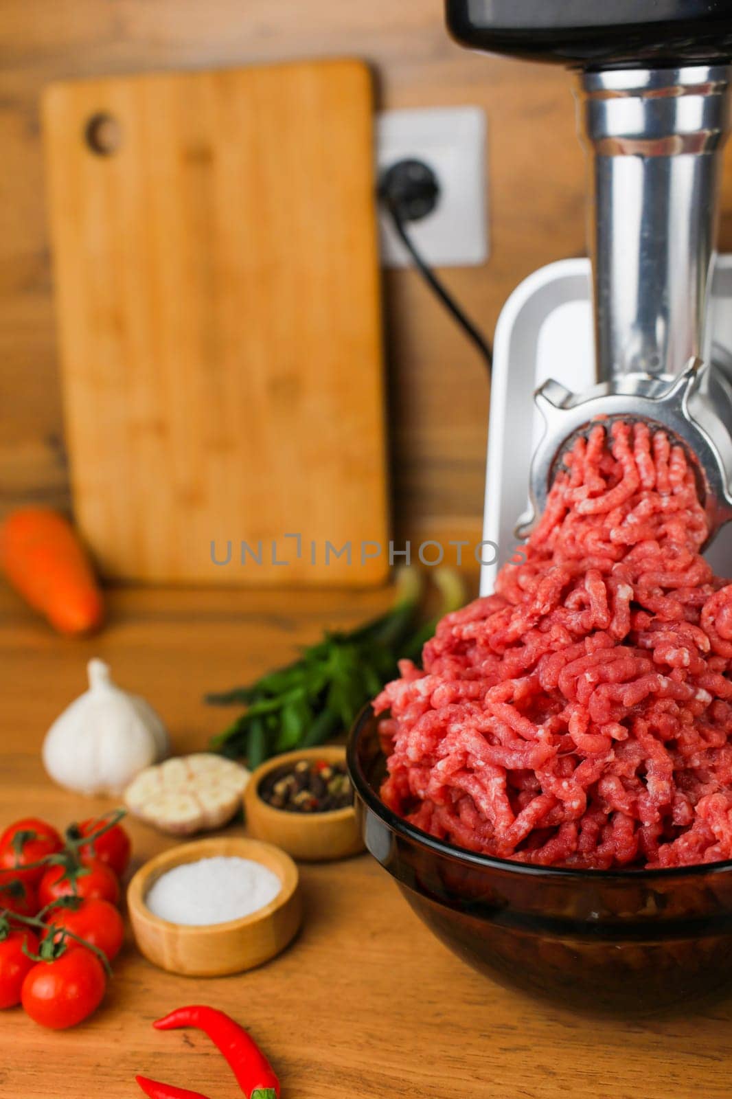 The concept of healthy eating, cooking. Side view on a wooden background: dark dishes with red minced meat inside, which comes out of a metal meat grinder, spices, herbs and vegetables are nearby. High quality photo