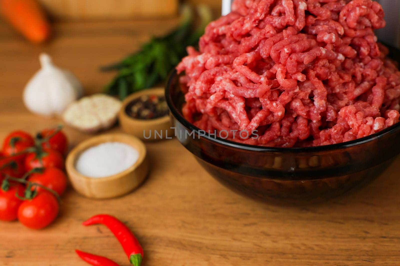 The concept of healthy eating, cooking. Close-up side view of a dark plate with red ground beef with fat streaks on a wooden background, spices, herbs and vegetables are standing next to it. High quality photo