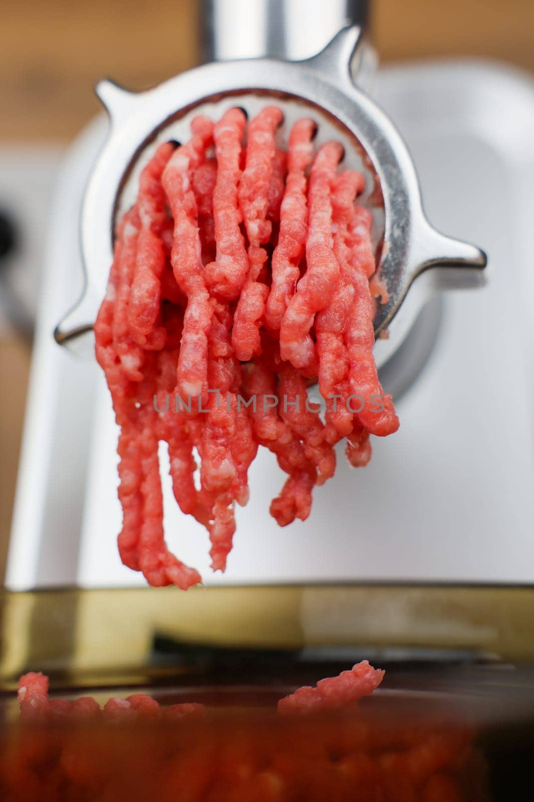 The concept of healthy and proper nutrition, cooking. Close-up side view of red ground beef with streaks of fat coming out of a metal grinder and falling into a transparent black plate below. High quality photo