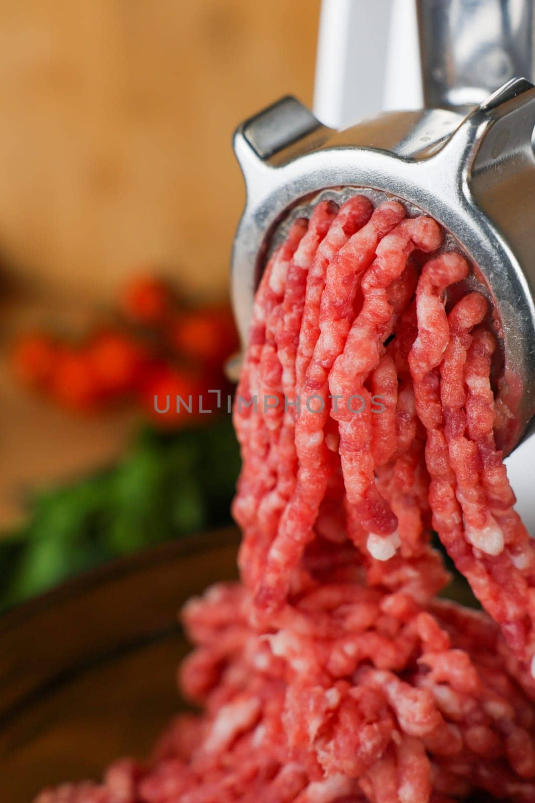 Concept of healthy and proper nutrition, cooking.Close-up of red ground beef with fat streaks coming out of a metal meat grinder on a wooden background, vegetables and herbs are visible out of focus. High quality photo