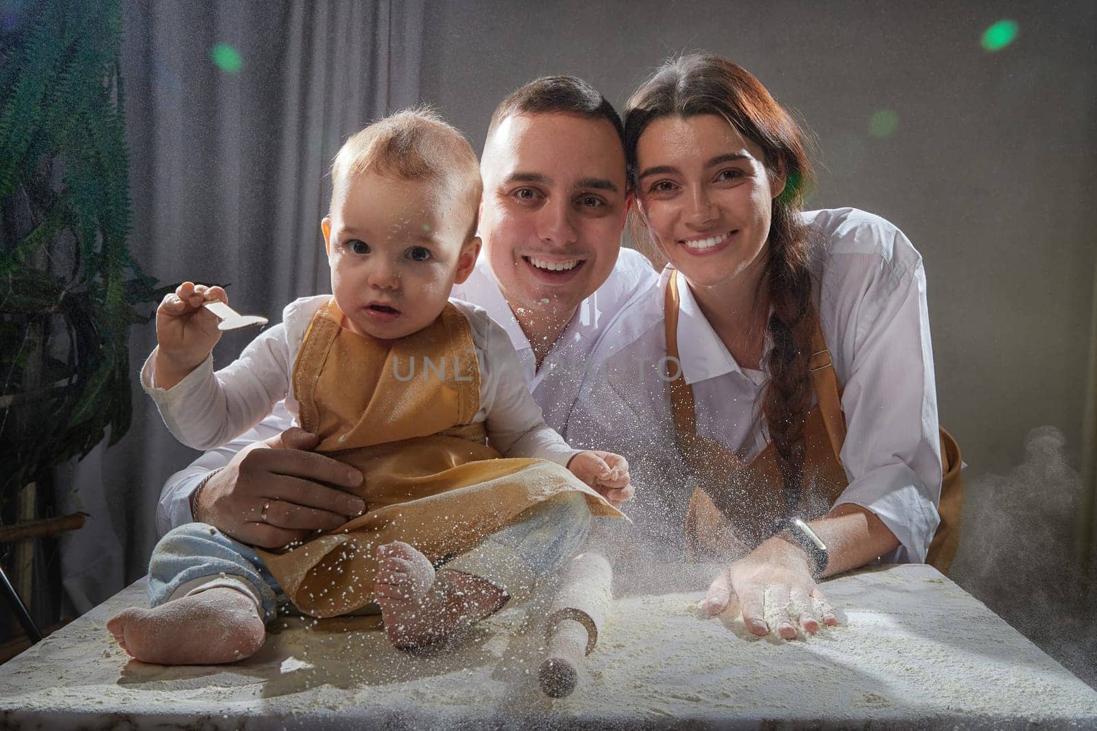 A family enjoys a fun cooking session, playfully covered in flour while engaging with their little ones in warm kitchen