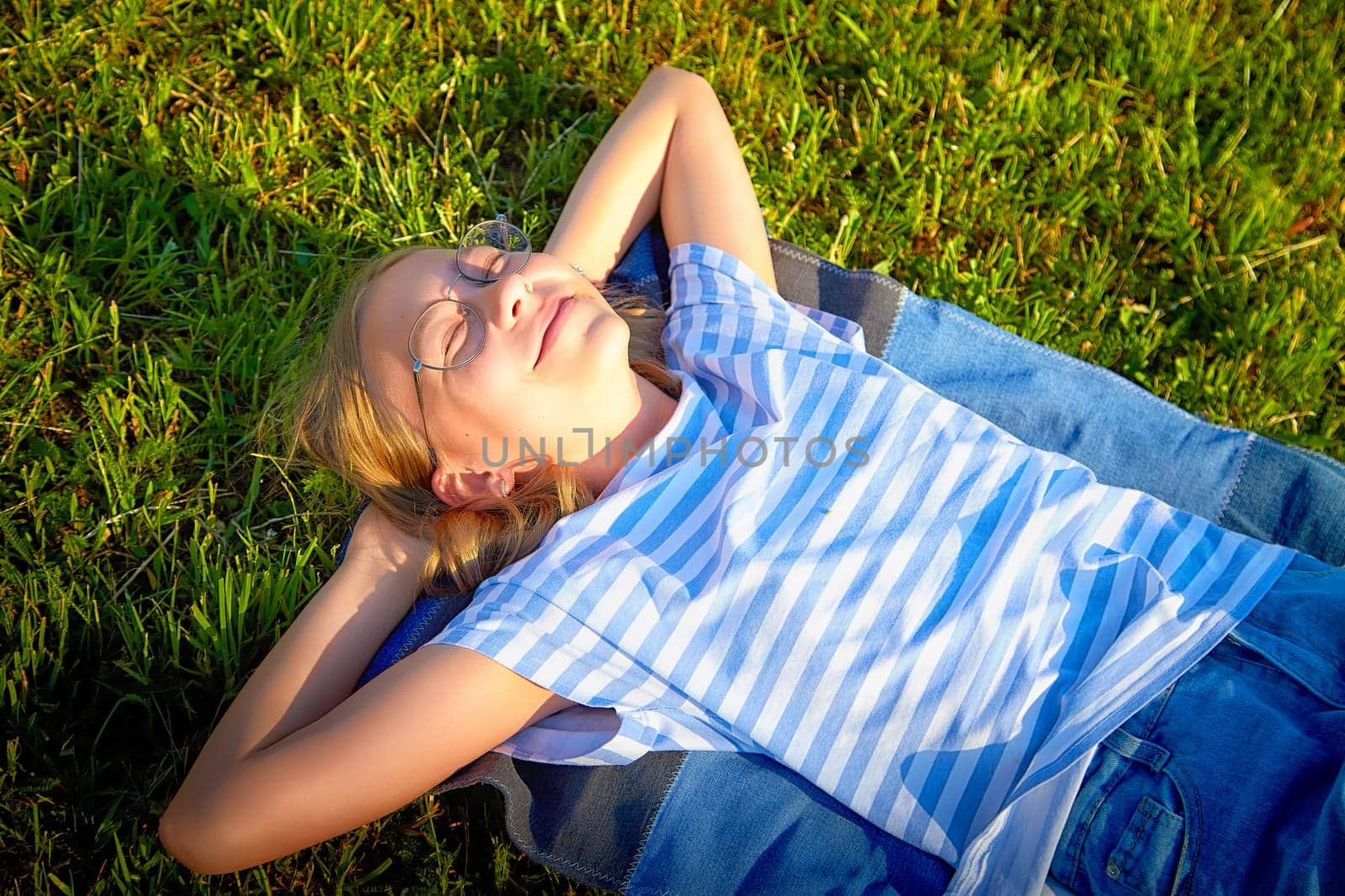 A child enjoys a peaceful moment lying down on a soft blanket while soaking up the sun in a green field.