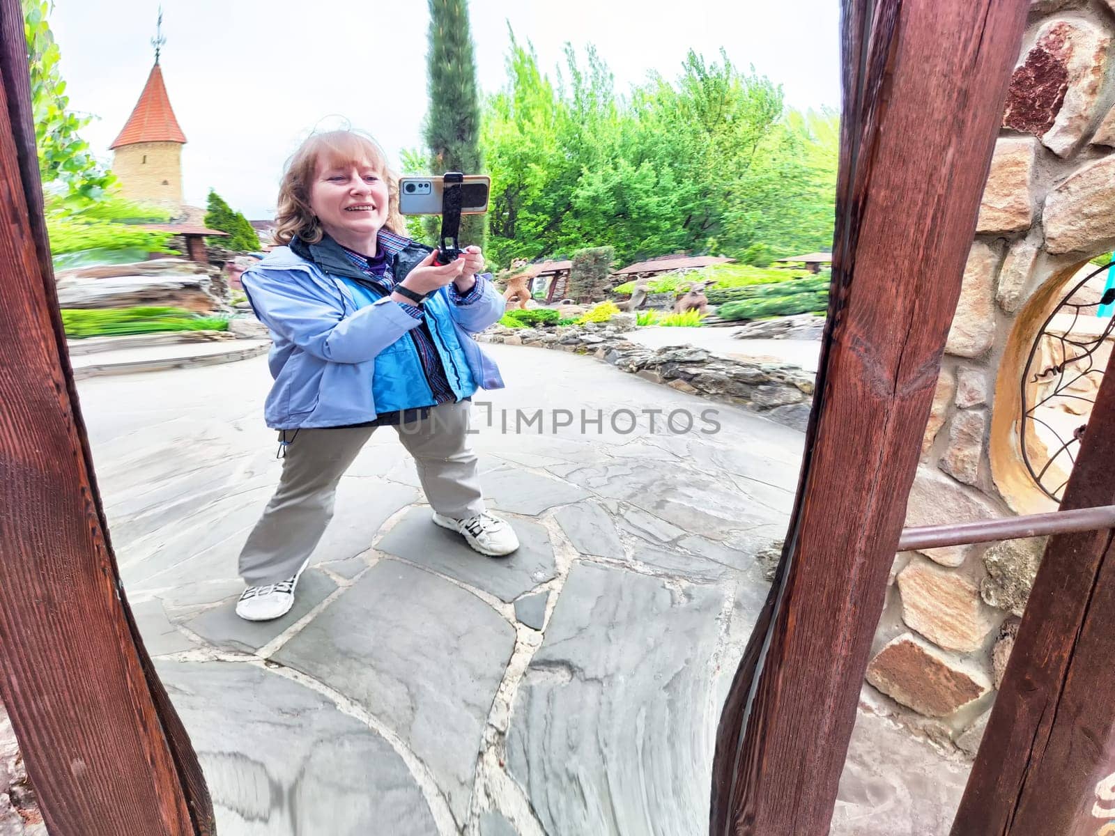 Blonde woman has fun taking a silly selfie in a distorted mirror while exploring a park filled with lush greenery.