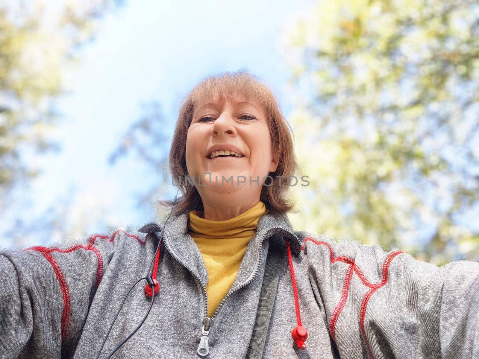 Blonde woman in a gray sweater smiles widely as she takes a selfie during her autumn adventure in nature.