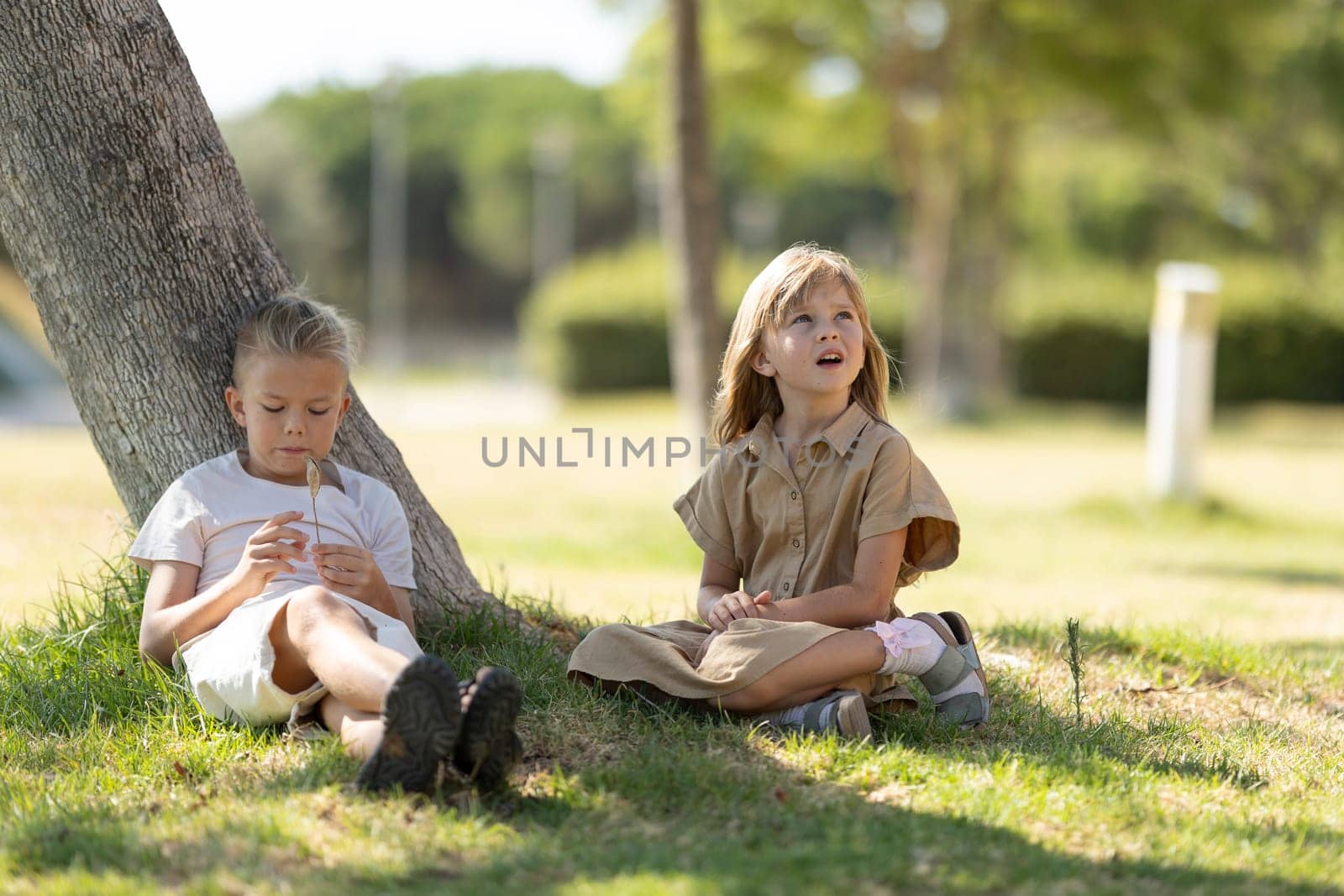 Two kids relaxing and playing under a tree on a sunny day