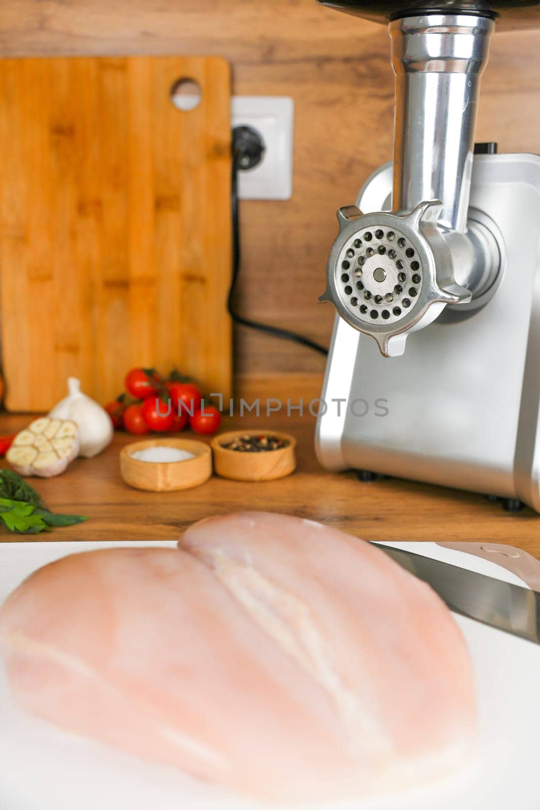 Chicken fillet lies on a white cutting board against the background of a meat grinder, vegetables and spices. The concept of dietary recipes, proper and healthy nutrition, the cooking process. High quality photo