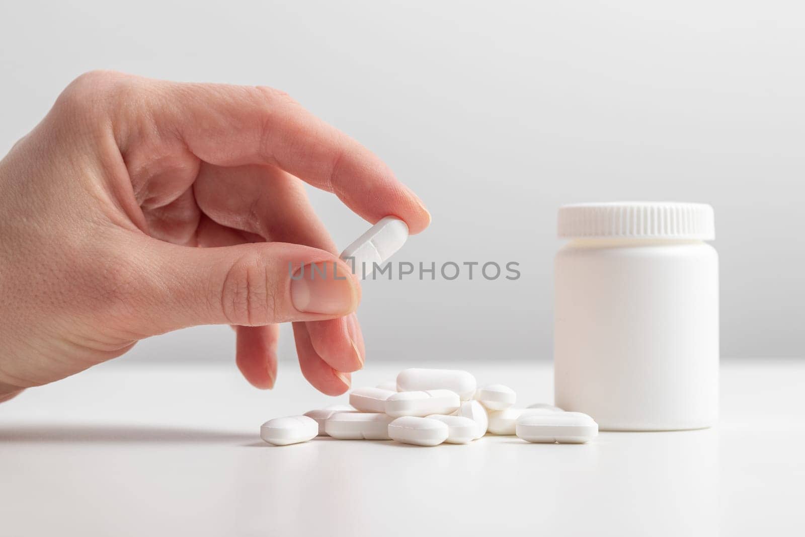Female taking medicine, holding white pill and a glass of water on white background. Concept of health care, dietary supplements, treatment of depression and diseases. High-quality photo