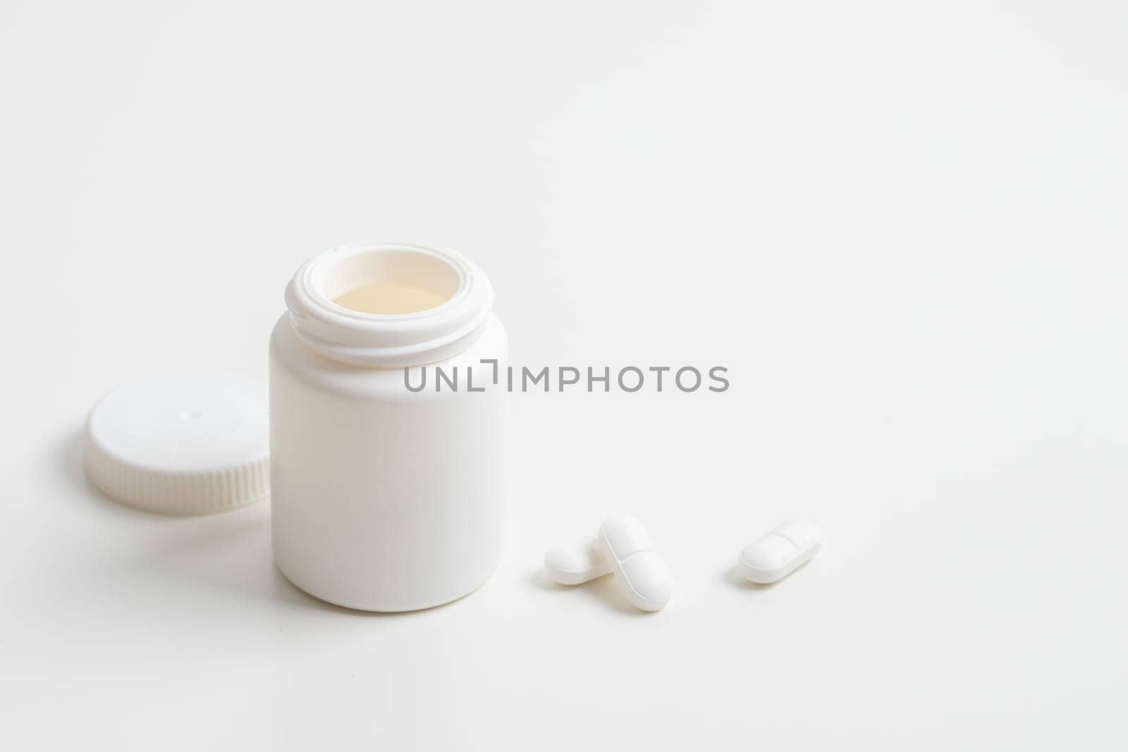 White pills and plastic medicine bottle on a white background with copy space. Medicine and health concepts include a jar with pills or vitamins. High-quality photo mock-up banner