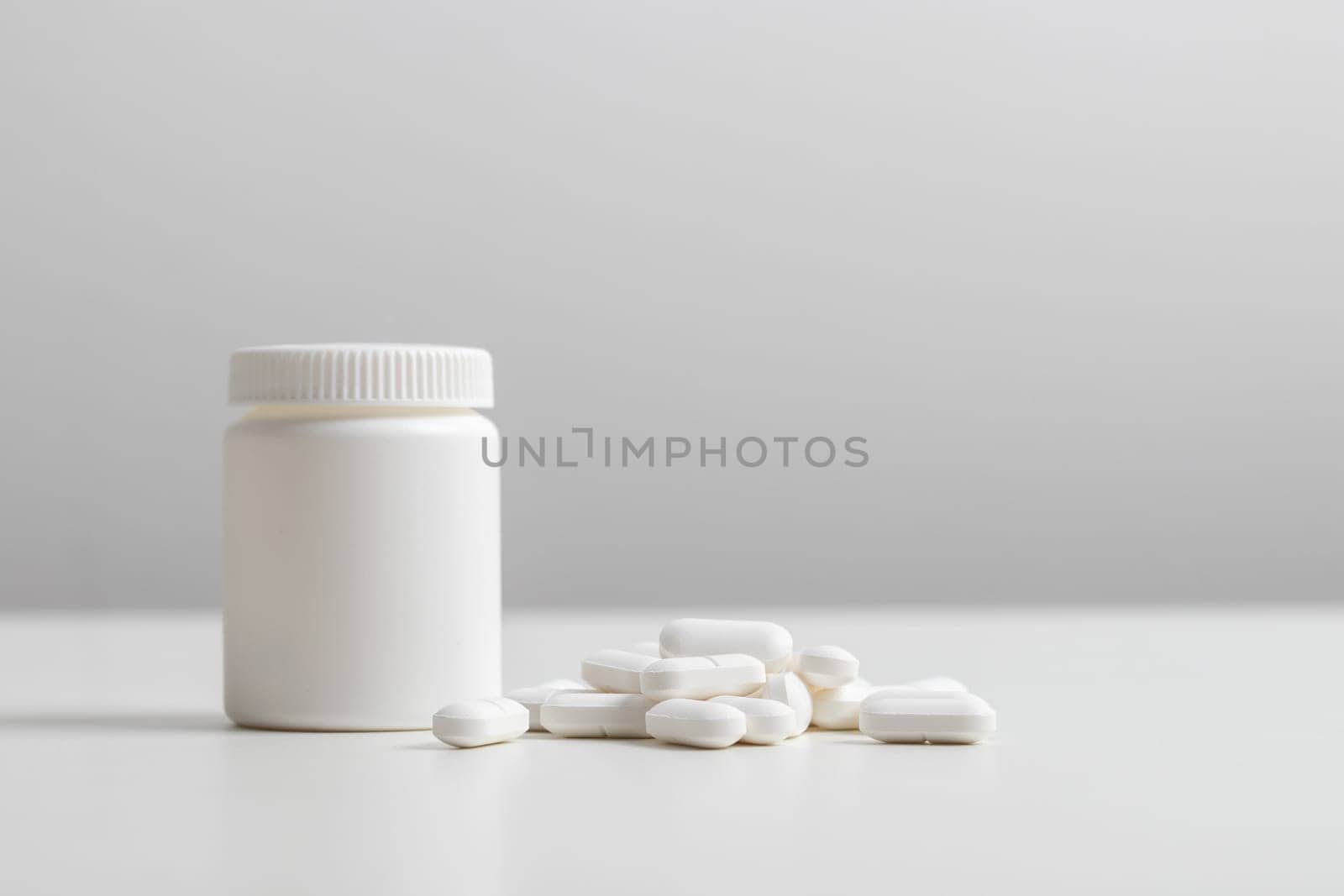 White pills and plastic medicine bottle on a white background with copy space. Medicine and health concepts include a jar with pills or vitamins. High-quality photo mock-up banner