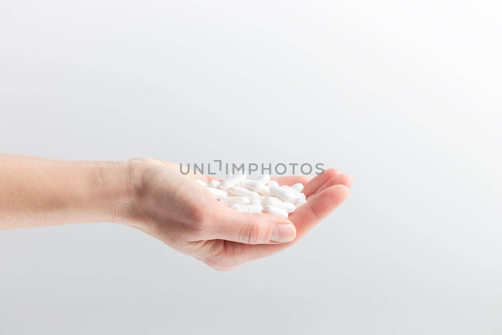 Female taking medicine, holding white pill and a glass of water on white background. Concept of health care, dietary supplements, treatment of depression and diseases. High-quality photo