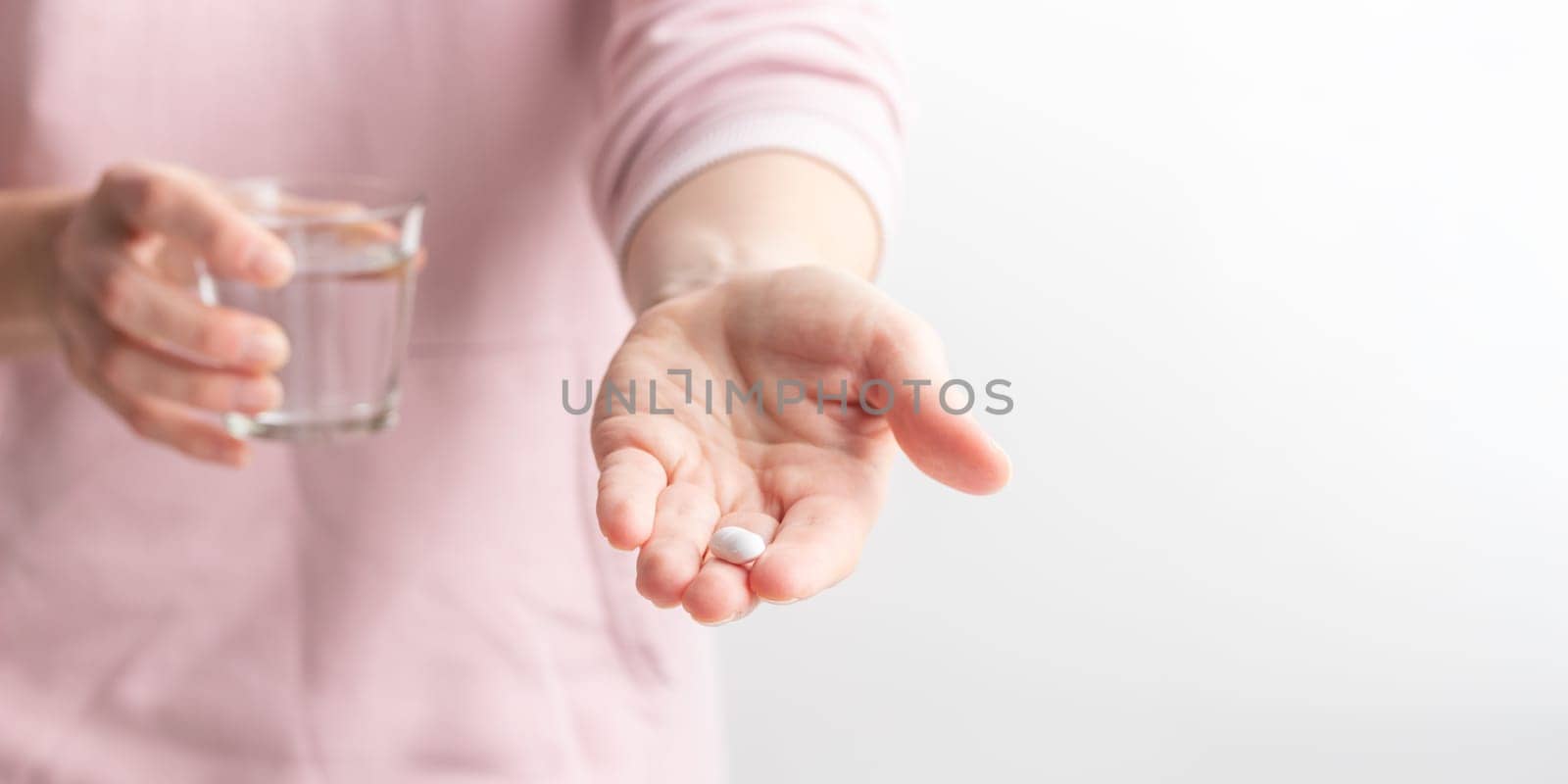 Female taking medicine, holding white pill and a glass of water on white background. Concept of health care, dietary supplements, treatment of depression and diseases. High-quality photo