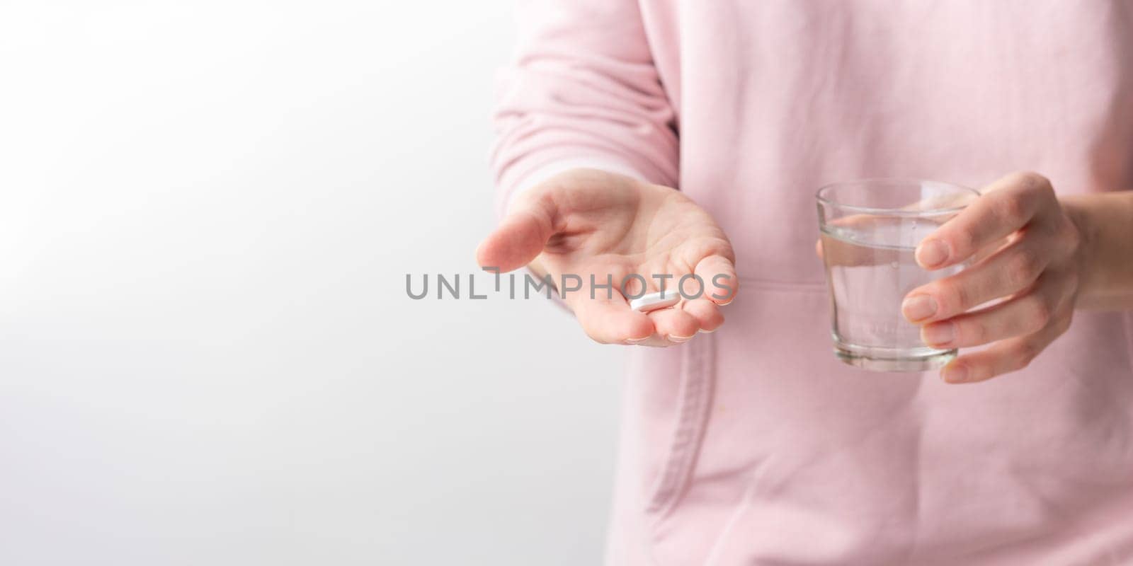 Female taking medicine, holding white pill and a glass of water on white background. Concept of health care, dietary supplements, treatment of depression and diseases. High-quality photo