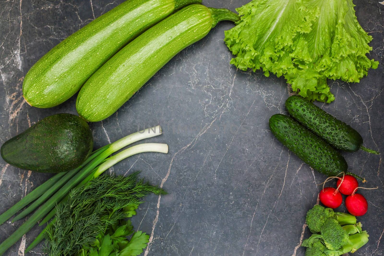 Vegetables, root vegetables and herbs lie against a background of dark marble around the edges with space for text in the center. The concept of cooking, proper nutrition, diet, and detox. High quality photo