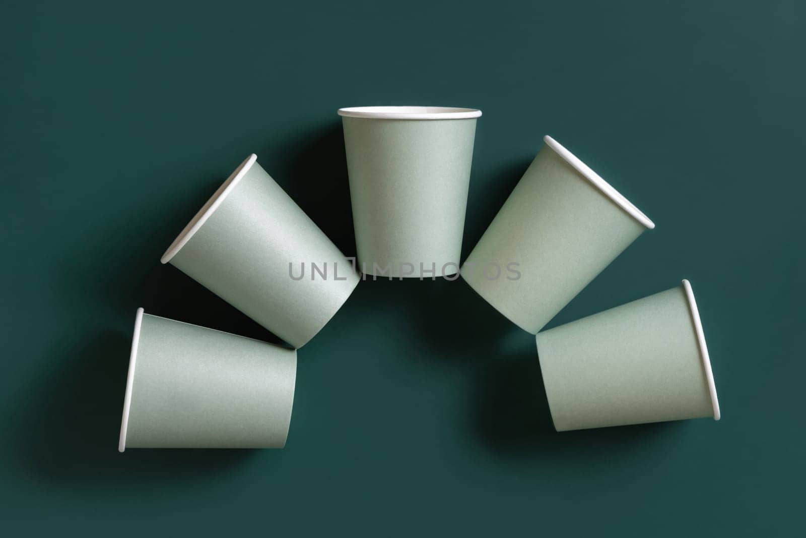 Disposable light green paper cups on a dark green background top view, mockup with advertising copy space. Empty cardboard coffee cups flat lay. No plastic and sustainable lifestyle concept