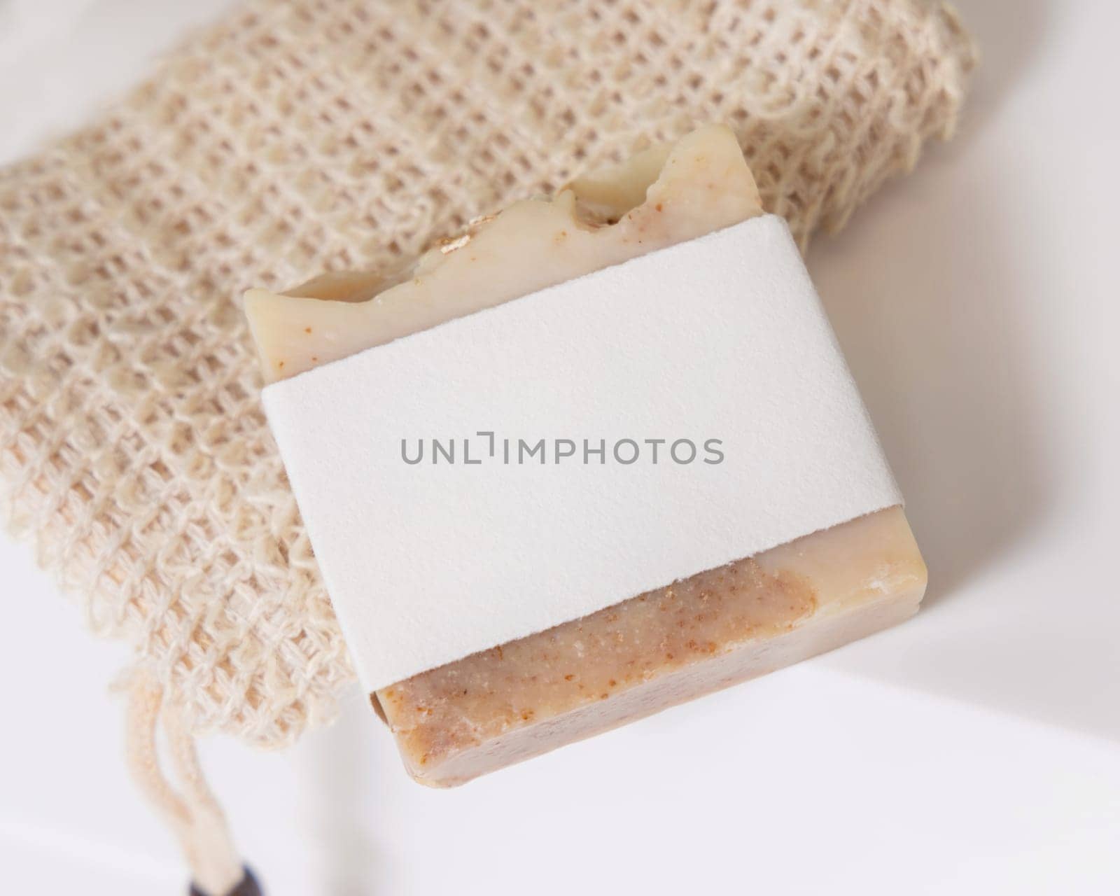Beige handmade soap bar with blank label on sisal soap saver bag on washbasin close up, packaging mockup, copy space. Natural herbal unbranded product for daily hygiene