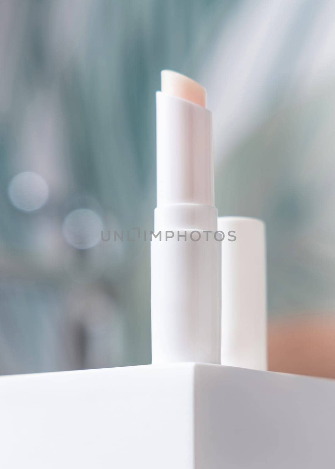 Opened white blank lip balm stick with a lid on basin in green tropical bathroom close up, packaging mockup with copy space. Lifestile scene with ubranded natural lipcare product