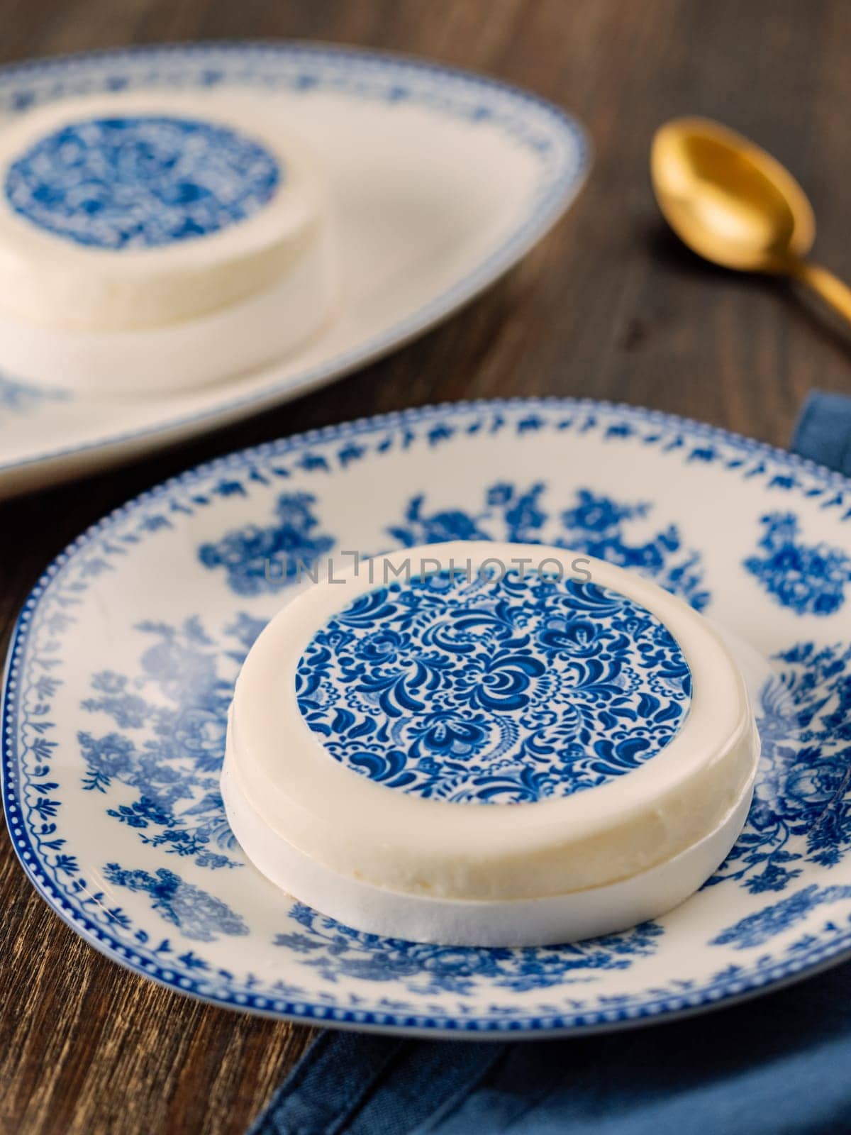 Pastry dessert in Gzhel rustic style. Sweet pastry decorated blue flowers photo printing on sugar paper. Mini cake Gzhel on plate over wooden tabletop background. Closeup. Vertical