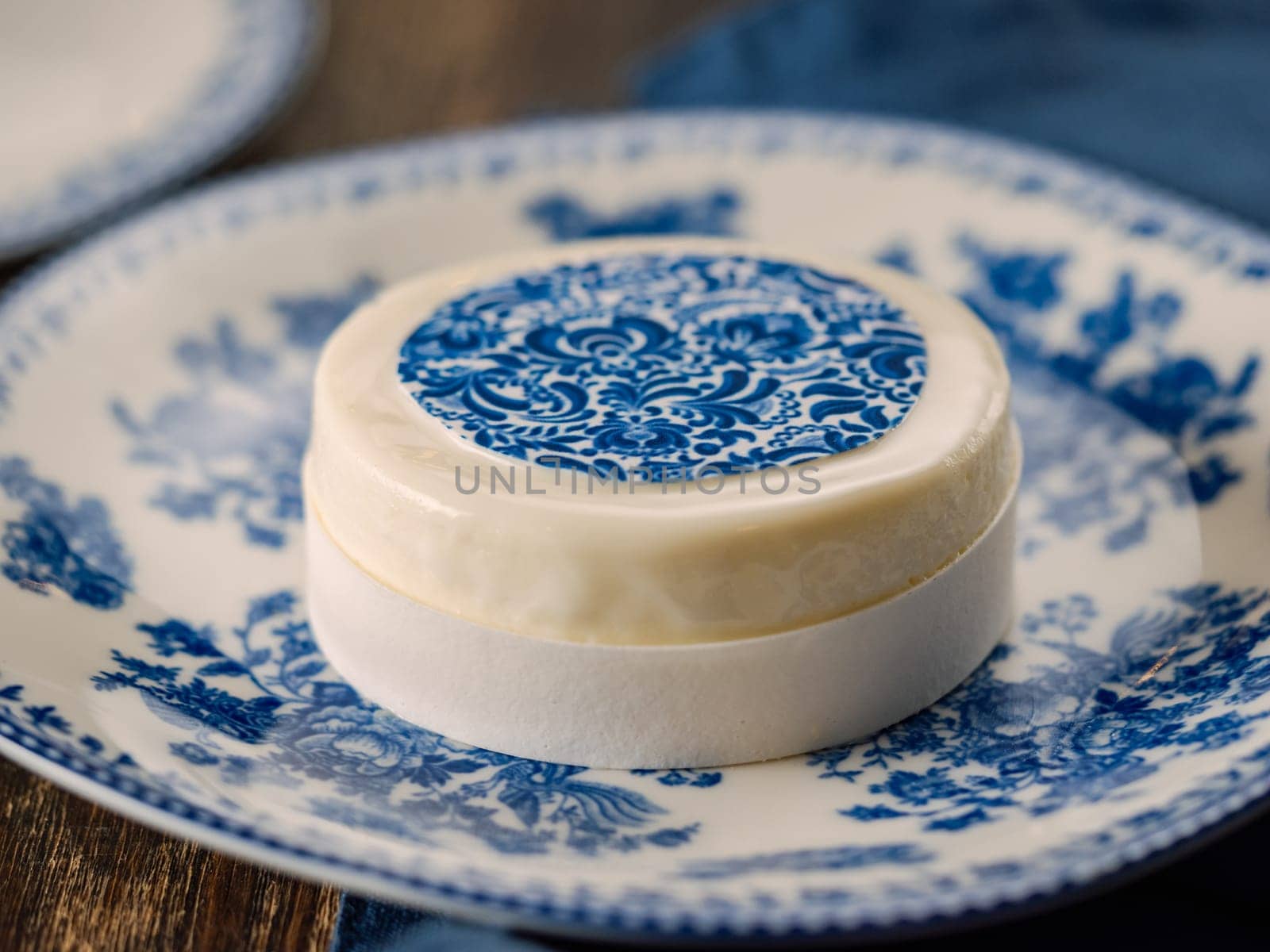 Pastry dessert in Gzhel rustic style. Sweet pastry decorated blue flowers photo printing on sugar paper. Mini cake Gzhel on plate over wooden tabletop background. Closeup