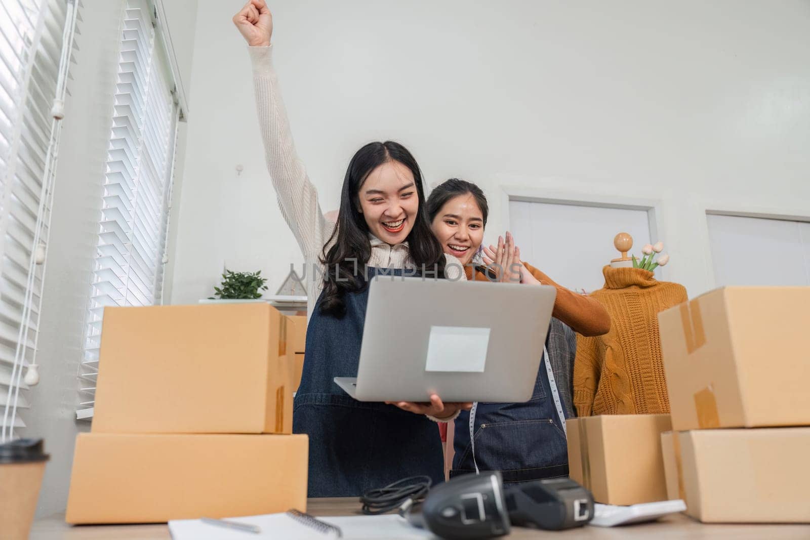 Two diverse retail workers joyfully celebrating an achievement with one raising their fist in excitement while using a laptop in a retail environment.