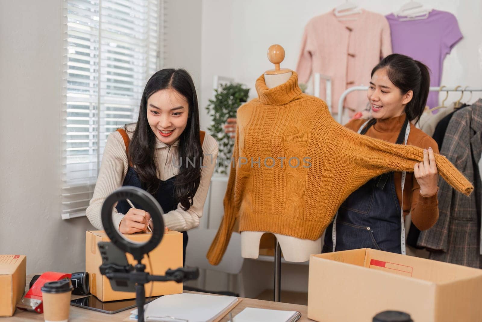 Two diverse retail workers presenting a stylish sweater on a mannequin while managing inventory and recording content for online sales in a store.