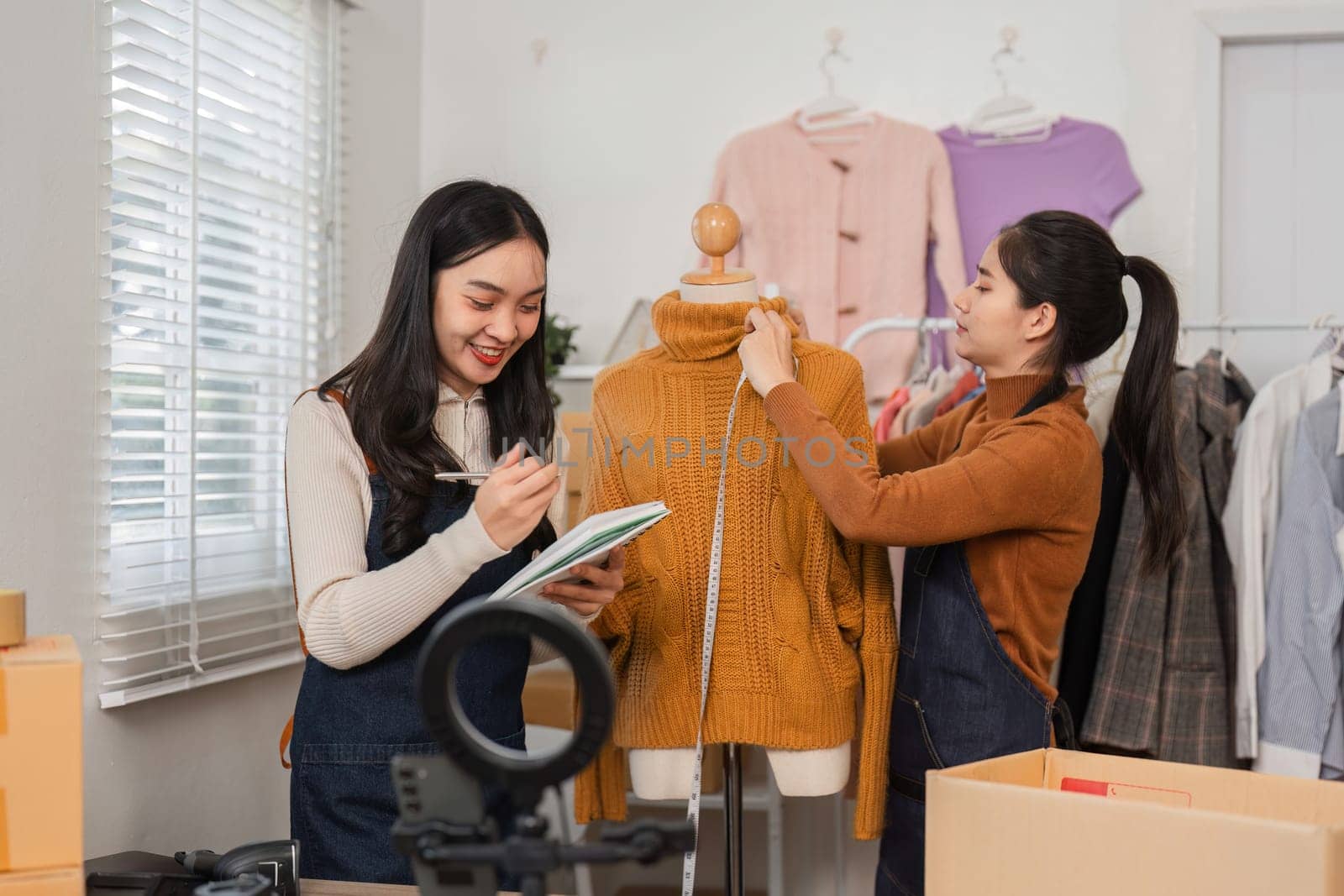 Two diverse retail workers collaborating to take notes and adjust a sweater on a mannequin while organizing inventory in a fashionable retail setting.