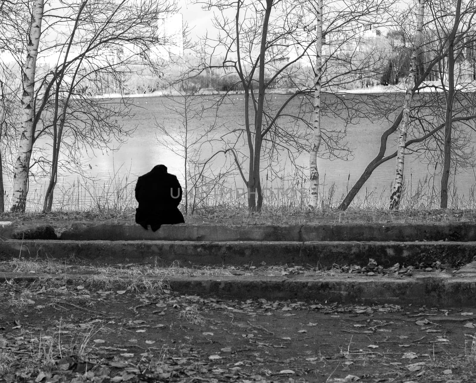Conceptual, black and white shot of the person sitting by the bank of the river