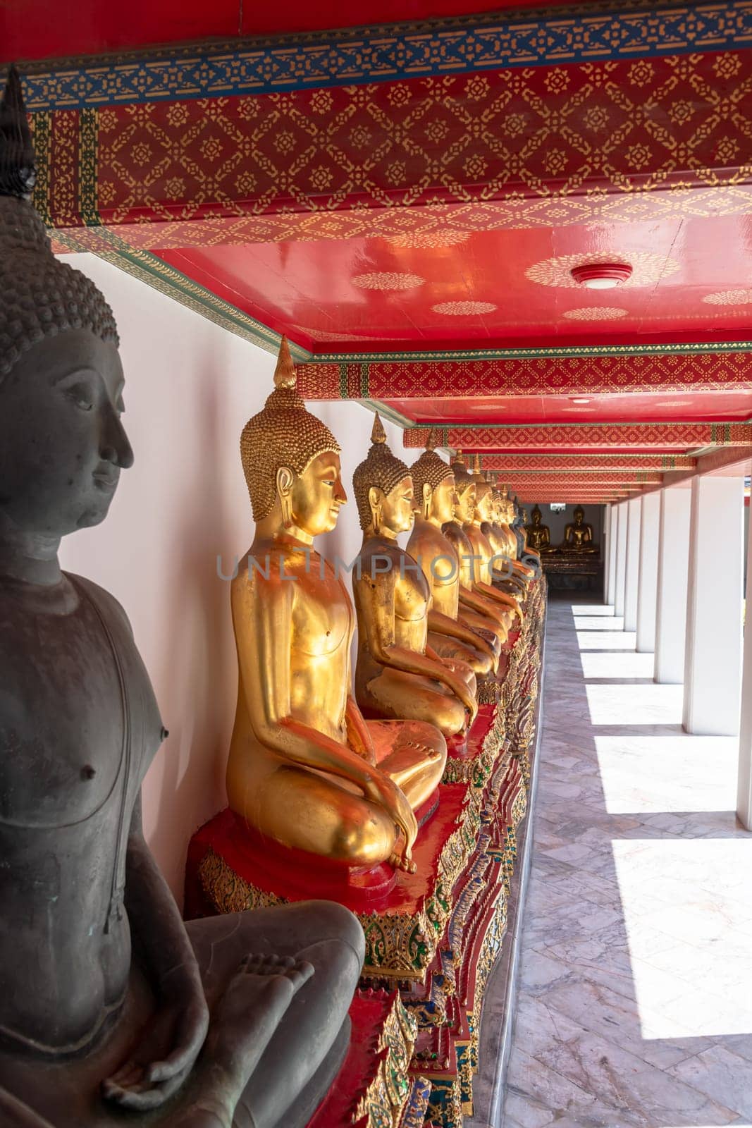 A tranquil corridor in a Buddhist temple, featuring golden statues and a vividly colored red ceiling