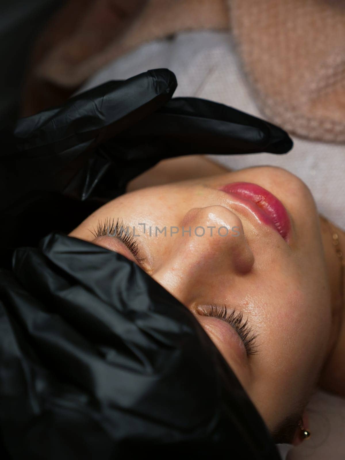 The beautician performs the procedure of microcurrents in black electric gloves to restore facial skin cells. Close-up, vertical