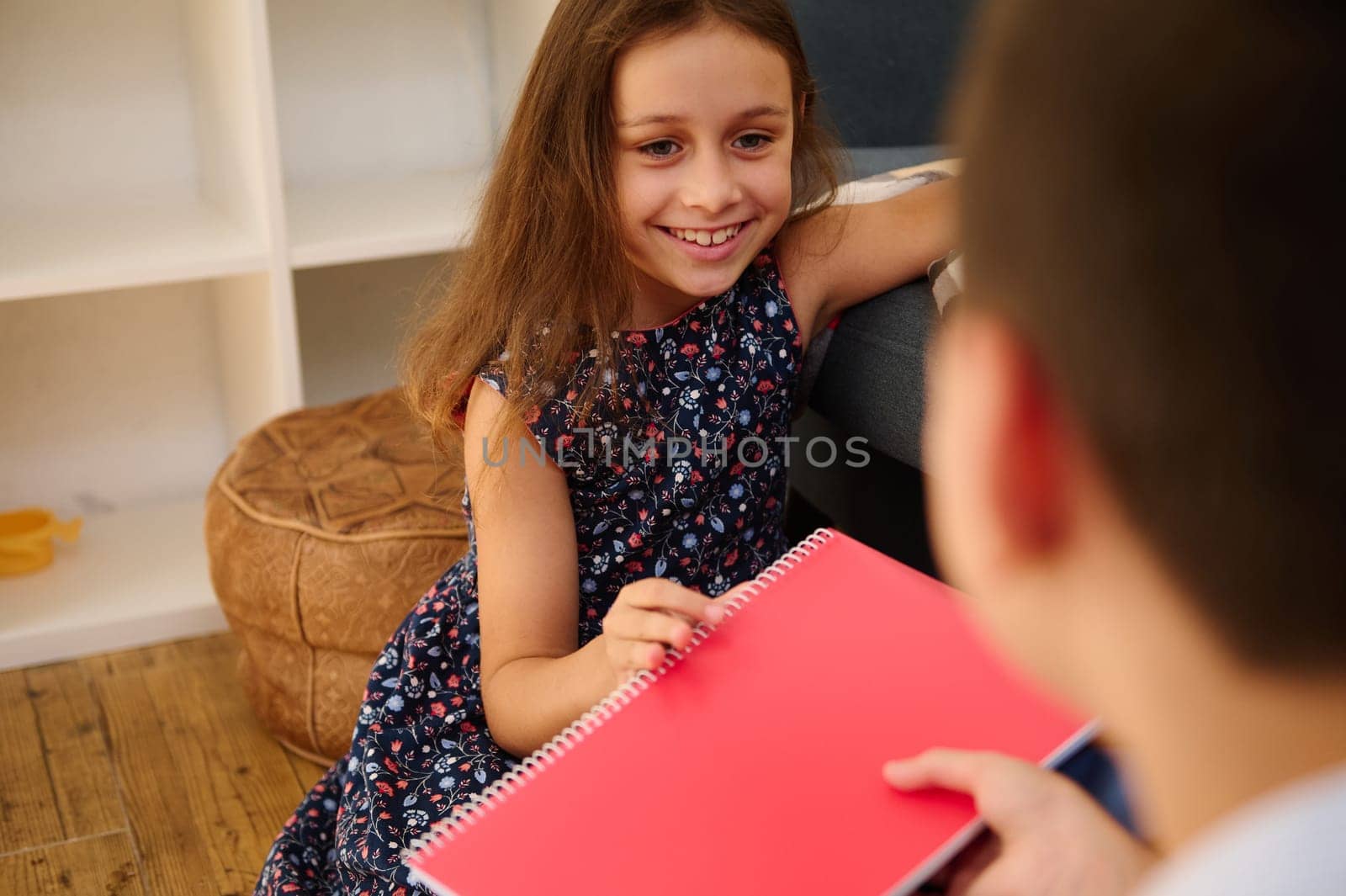 A cheerful girl sitting on a sofa, happily sharing a notebook with a friend, indoors.