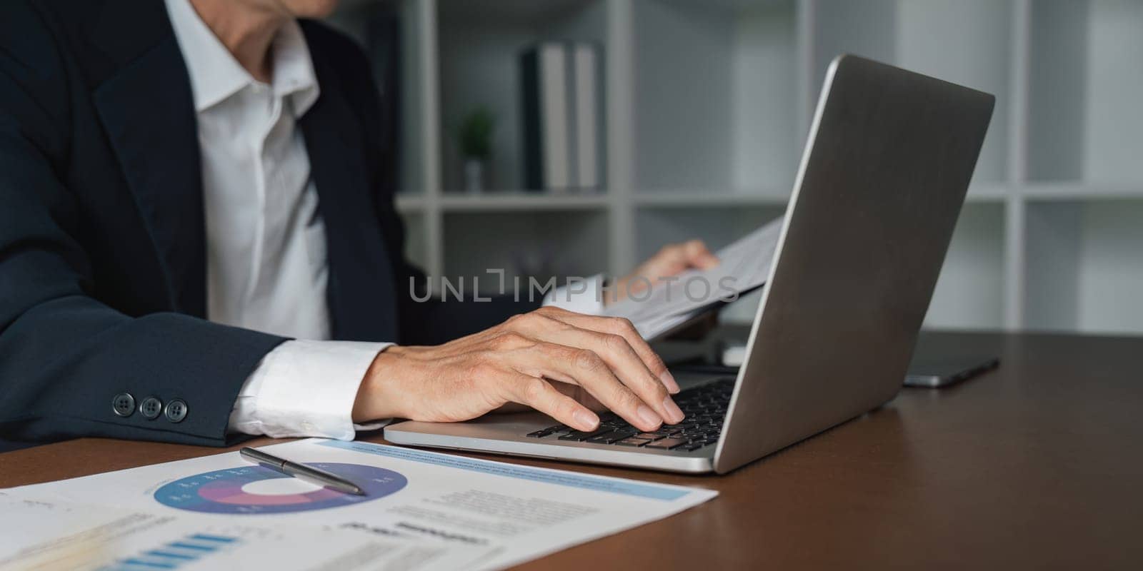 An elderly businessman reviews important reports on his laptop emphasizing the significance of diligence in a professional setting.