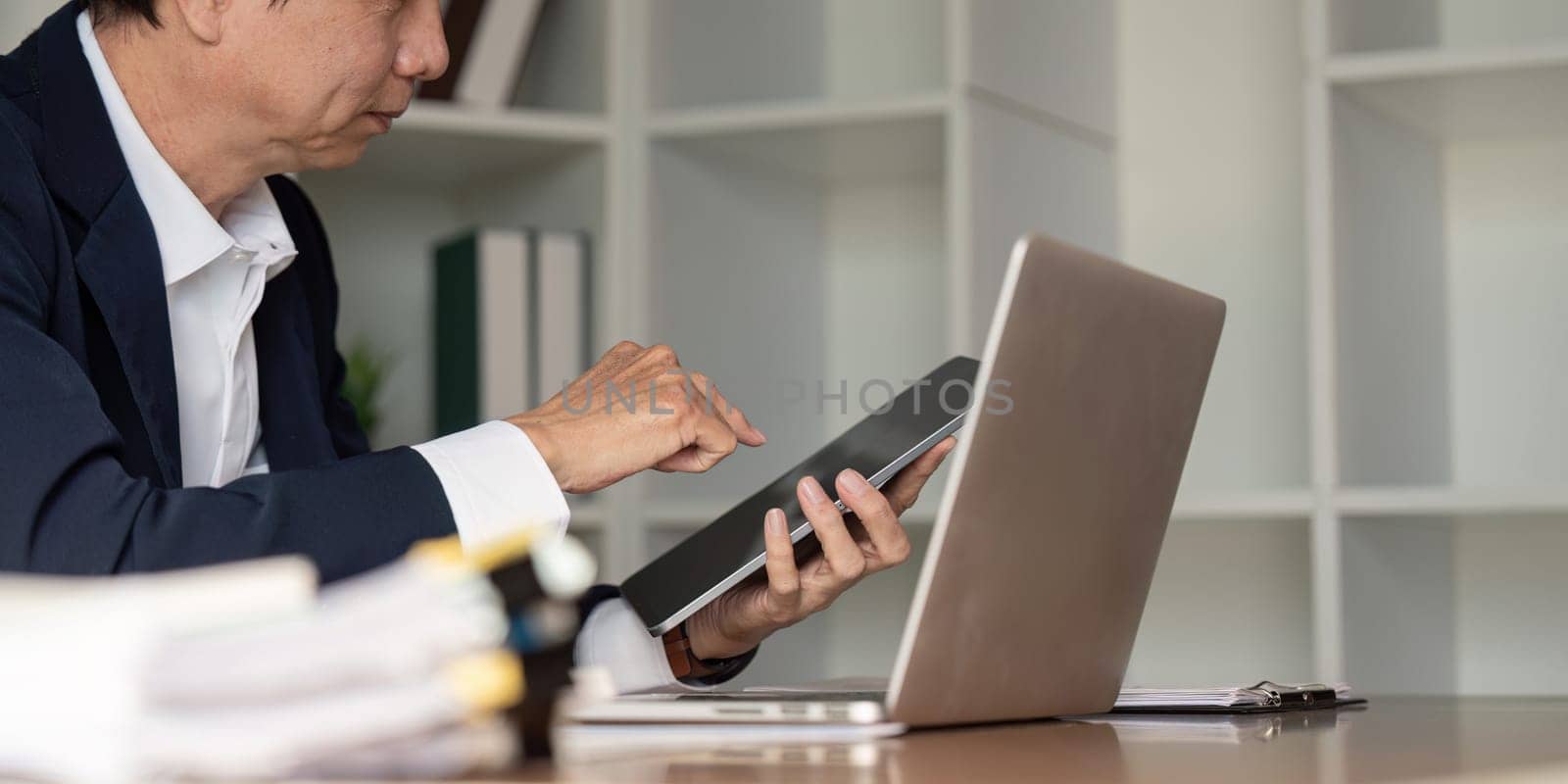 An elderly businessman reviews data on a tablet in a sleek office reflecting on strategic decisions in a digital age.