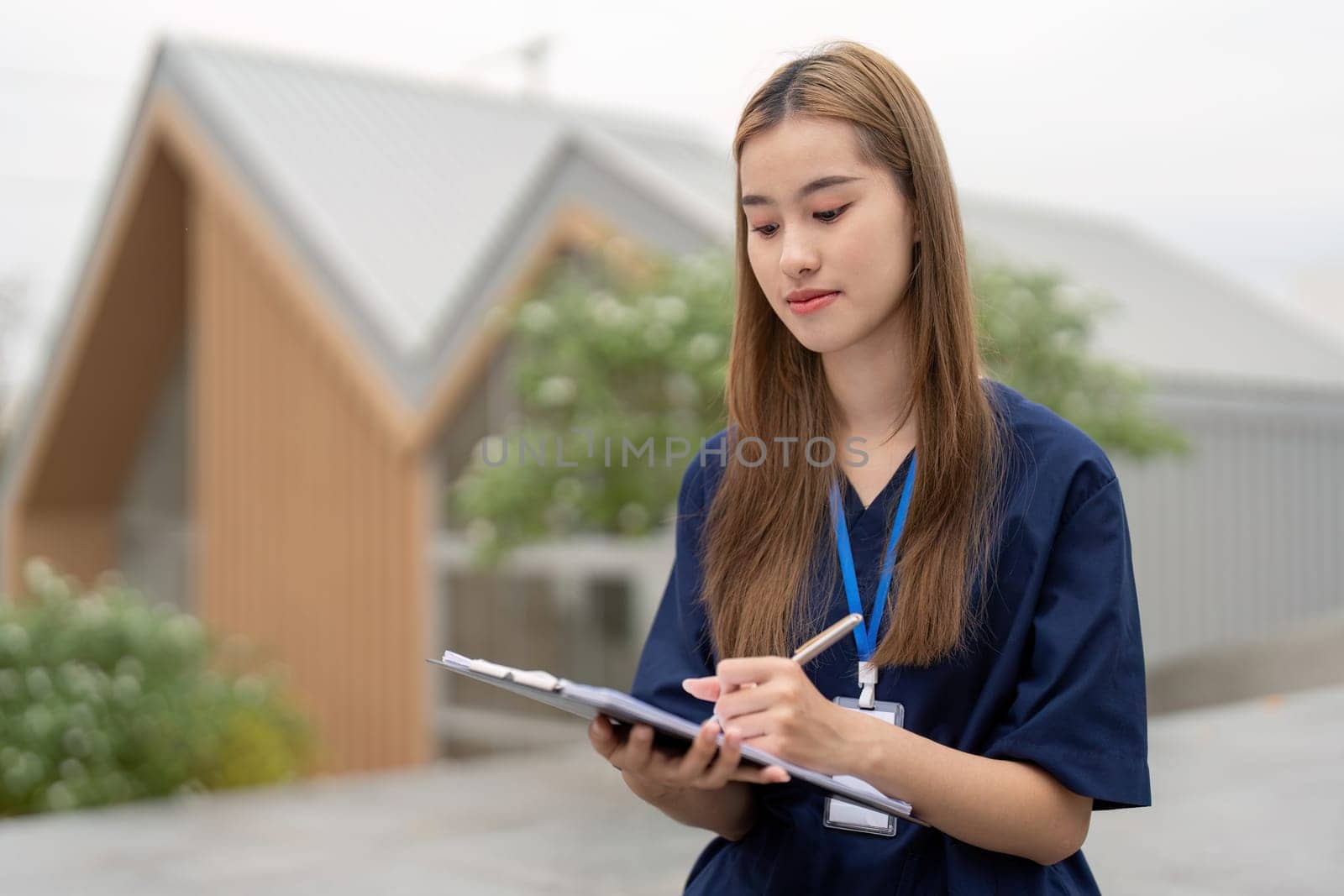 A focused female healthcare professional in scrubs writes on a clipboard outdoors, emphasizing the importance of relaxation and concentration in her medical practice.
