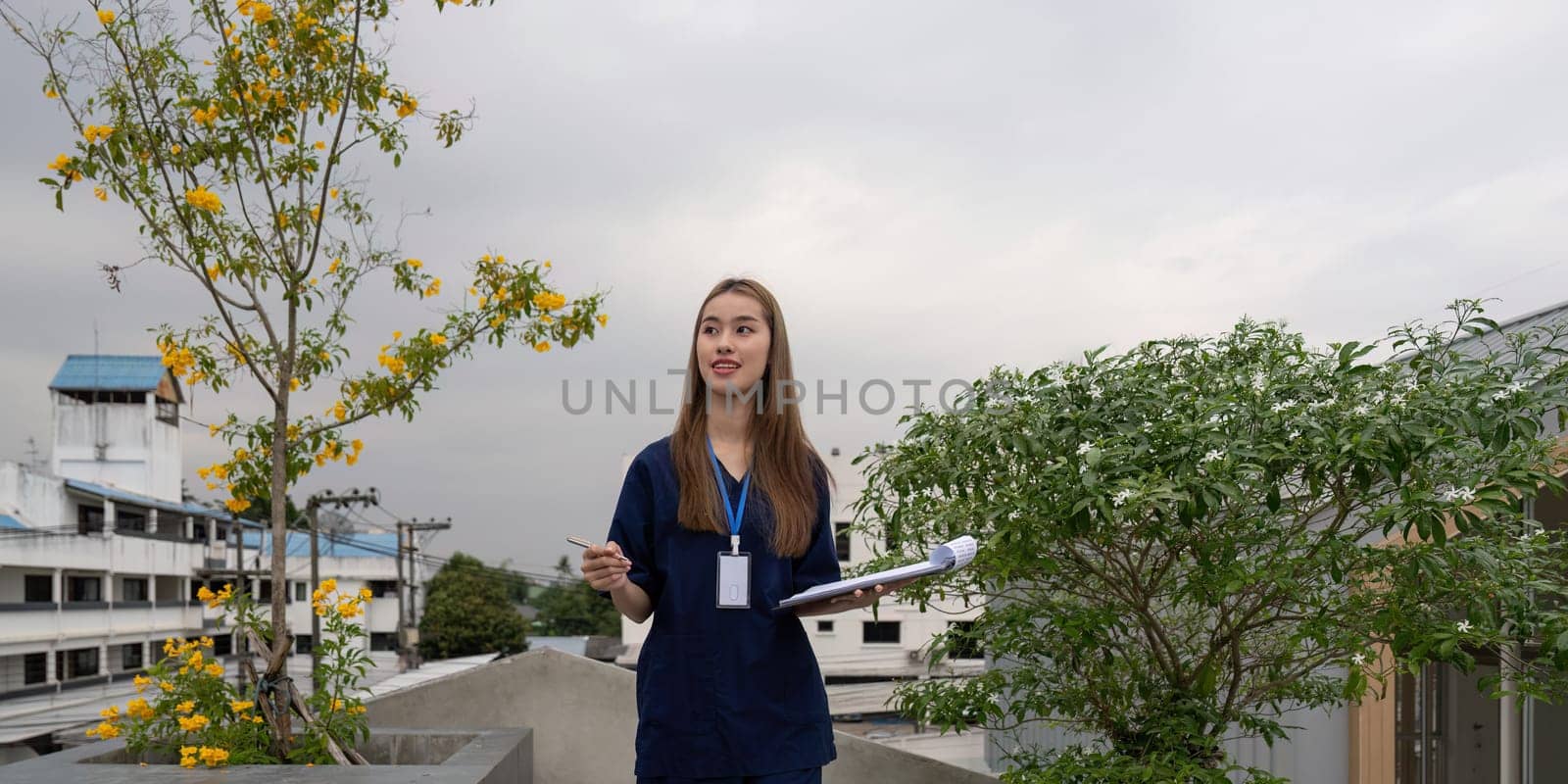 A smiling female healthcare professional in scrubs stands outdoors with a clipboard, showcasing the importance of relaxation and effective communication in her role.
