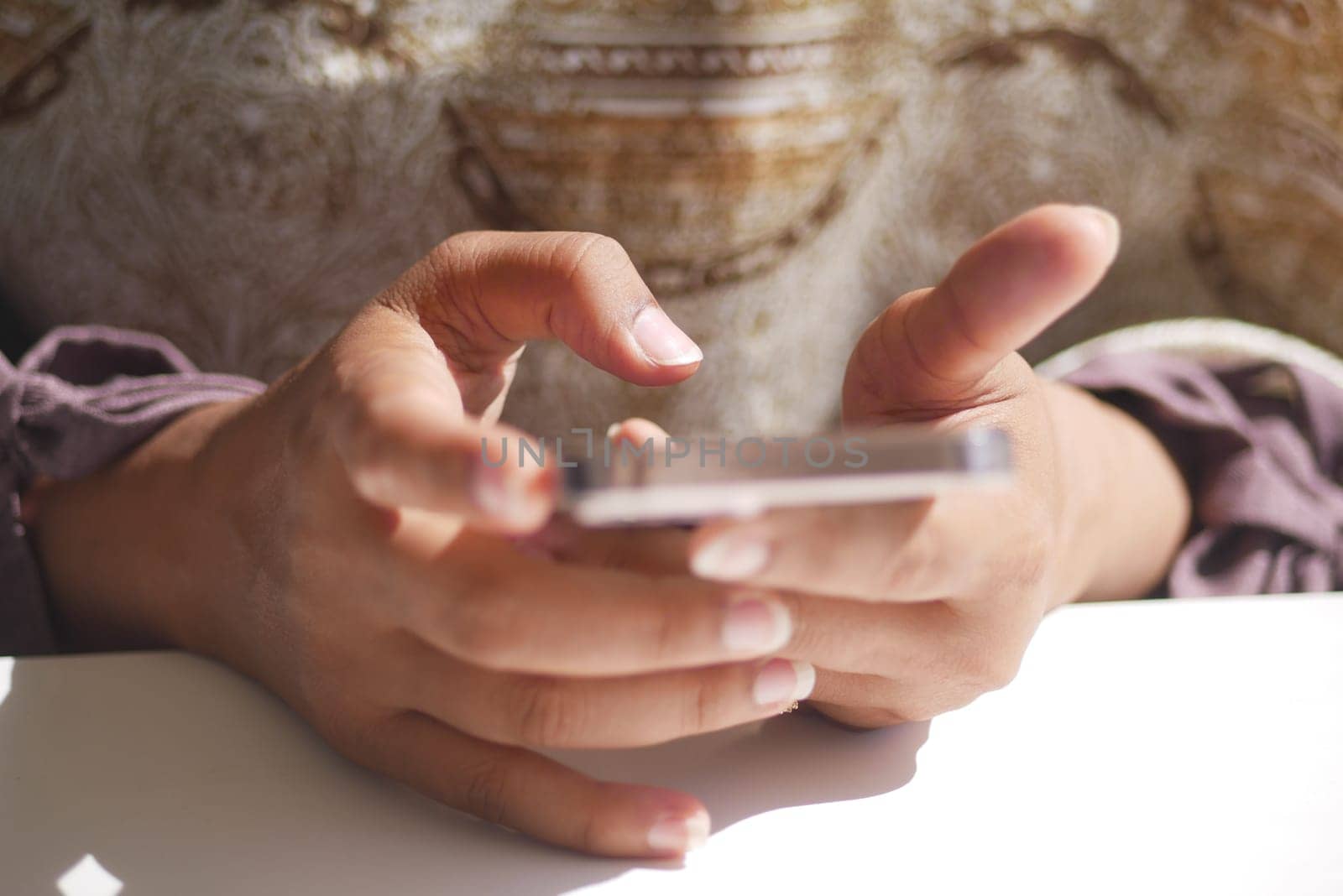 A person uses a smartphone while seated at a table in daylight.