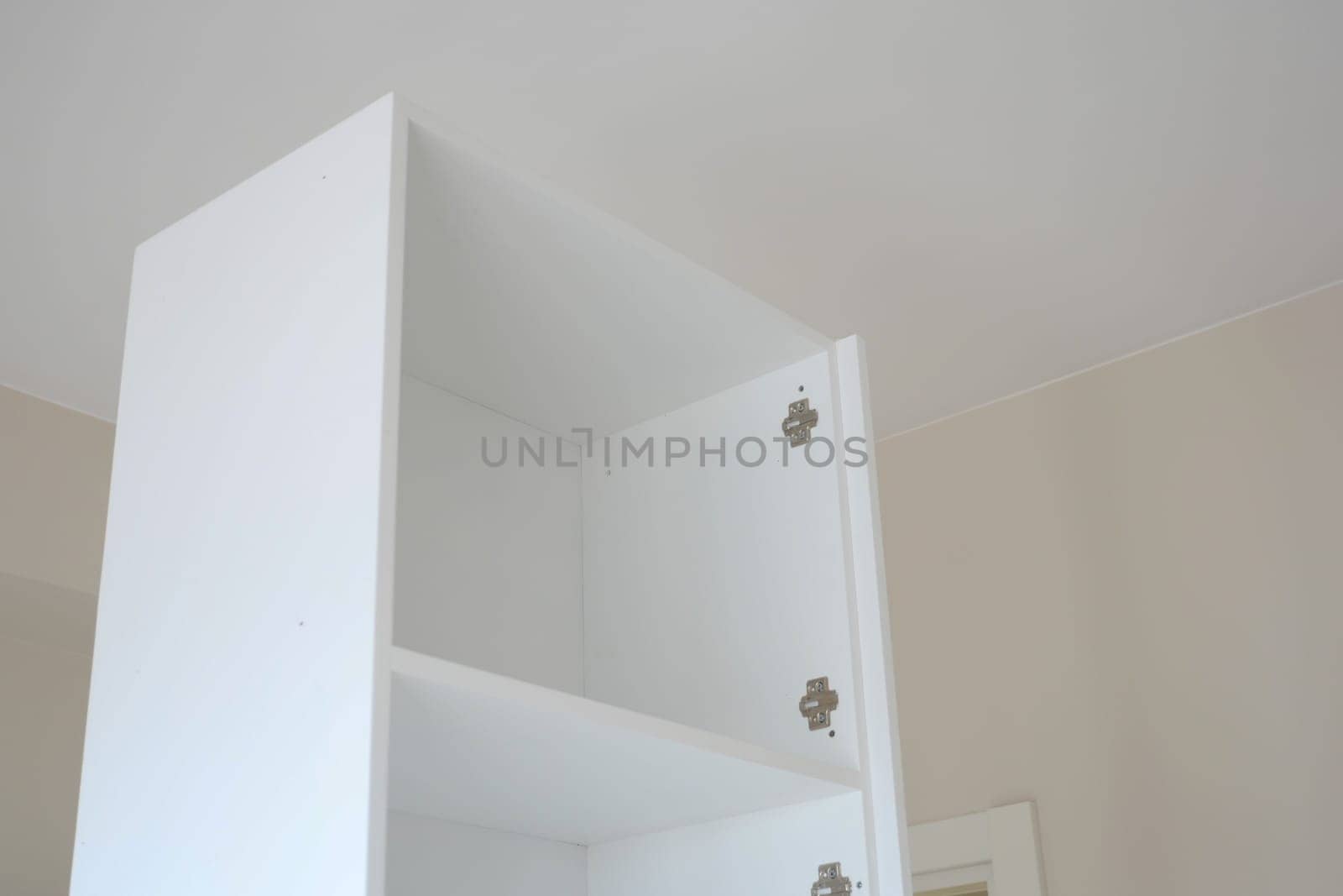 A white cabinet stands in a well-lit room with empty shelves.
