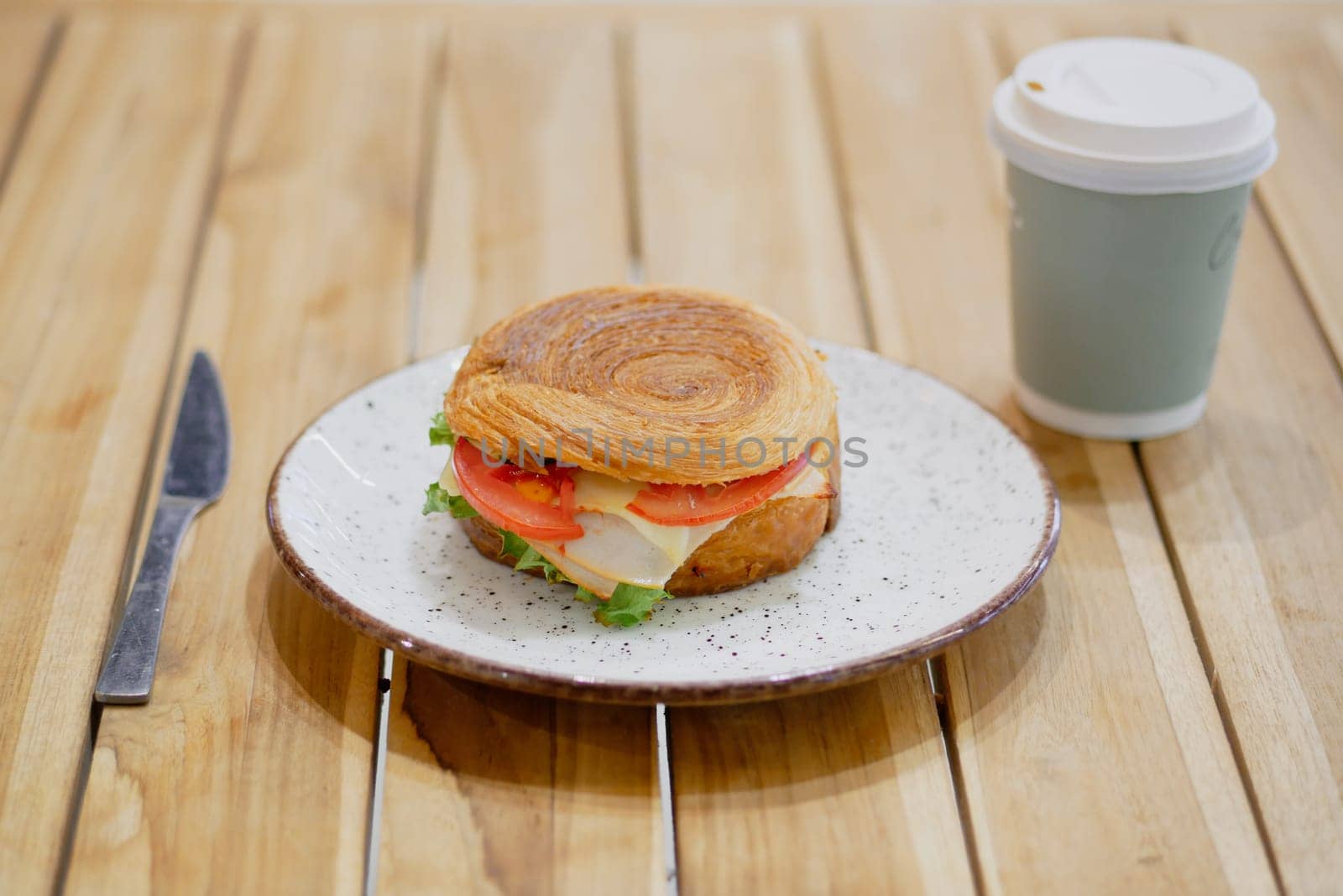 Delicious sandwich with layers of turkey, lettuce, and tomato beside coffee.