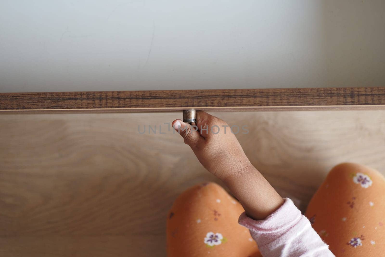 A child's hand grips a drawer handle while sitting on the floor.