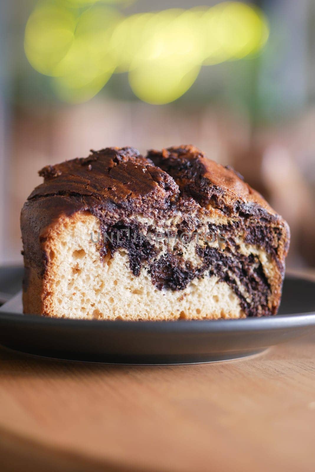 A slice of marbled cake sits on a black plate in a warm cafe setting.