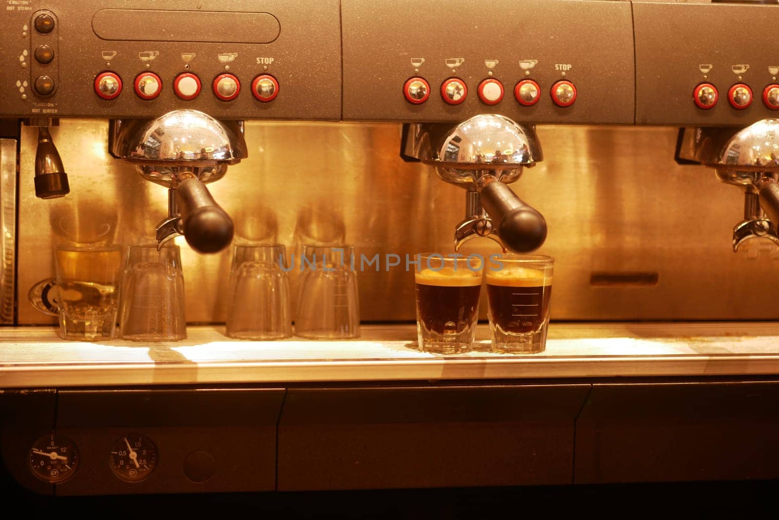 Two cups of freshly brewed espresso sit beneath a coffee machine in use.