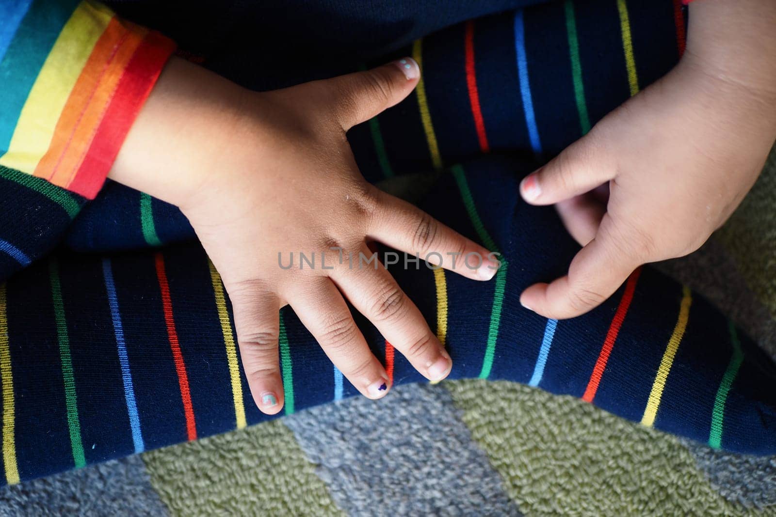 Small hands rest on vibrant striped socks while seated on a textured carpet.