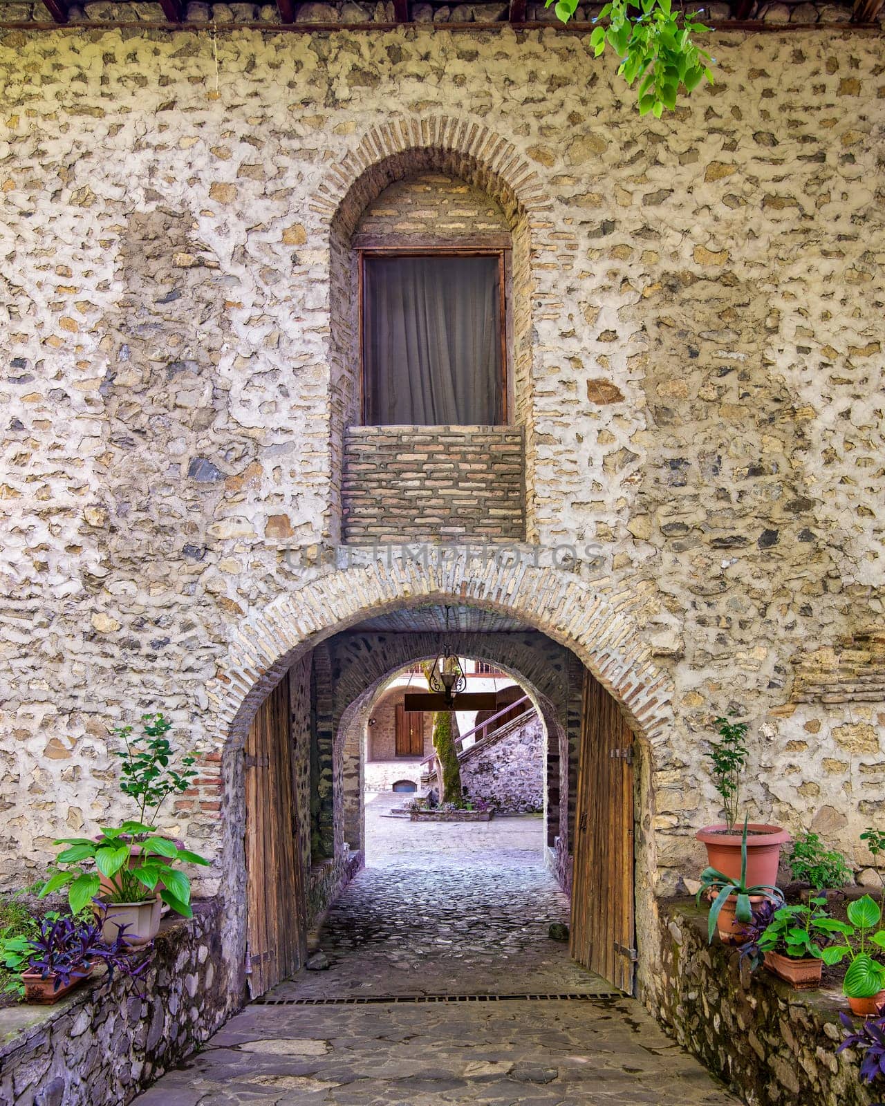 Arched entrance leading to the courtyard of the Upper Caravanserai in Shaki, Azerbaijan, with stone walls and lush greenery