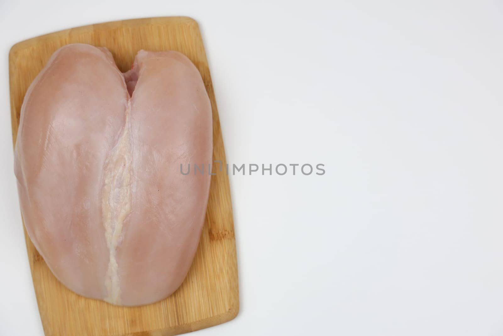 Close-up view of chicken fillet from above lying on a wooden cutting board on a white background with space for text. The concept of cooking, dietary menu, healthy and natural products. High quality photo