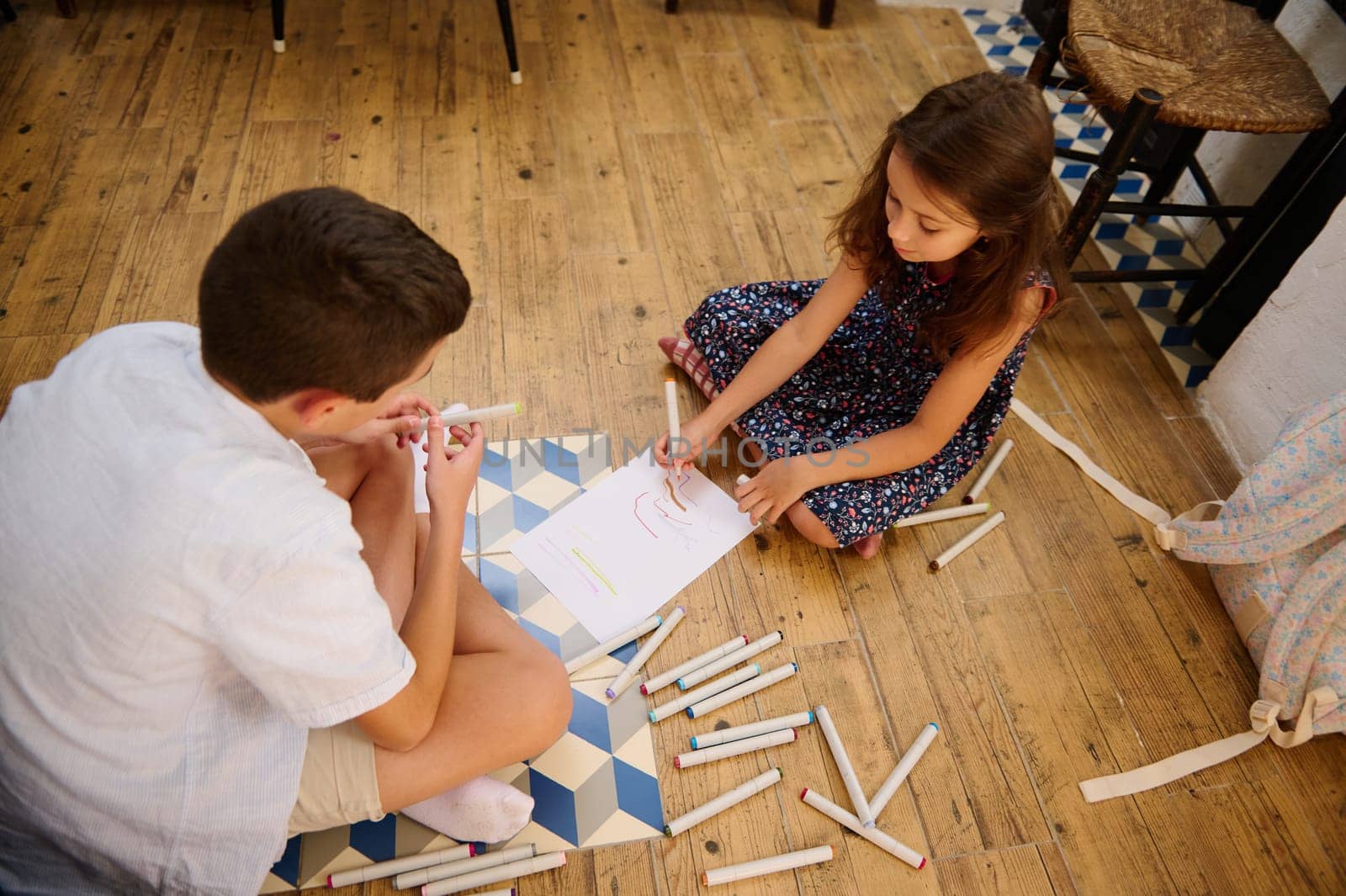 Two children are creating art together indoors, using markers and paper, fostering creativity and collaboration. The warm atmosphere reflects friendly learning and childhood enjoyment.