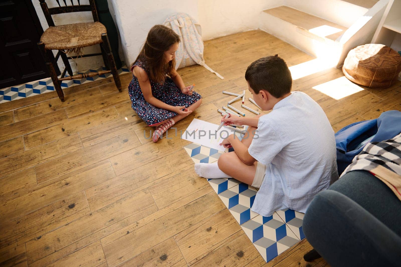 Two children engaged in creative activities, sitting on the floor with art supplies, enjoying a cozy indoor atmosphere. A bonding moment promoting creativity and sibling connection.