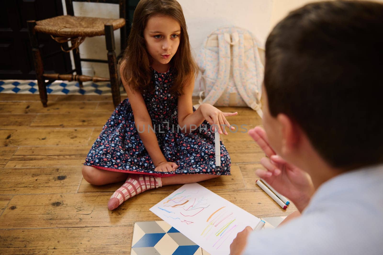 A young girl and boy enjoy drawing and discussing on the floor, sharing creativity.