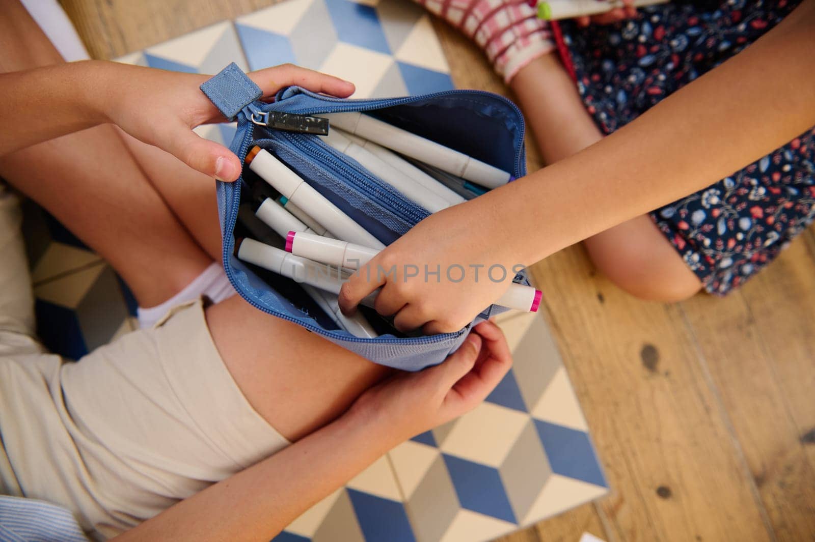Two children organizing colorful markers inside a blue pencil case, emphasizing creativity and collaboration.